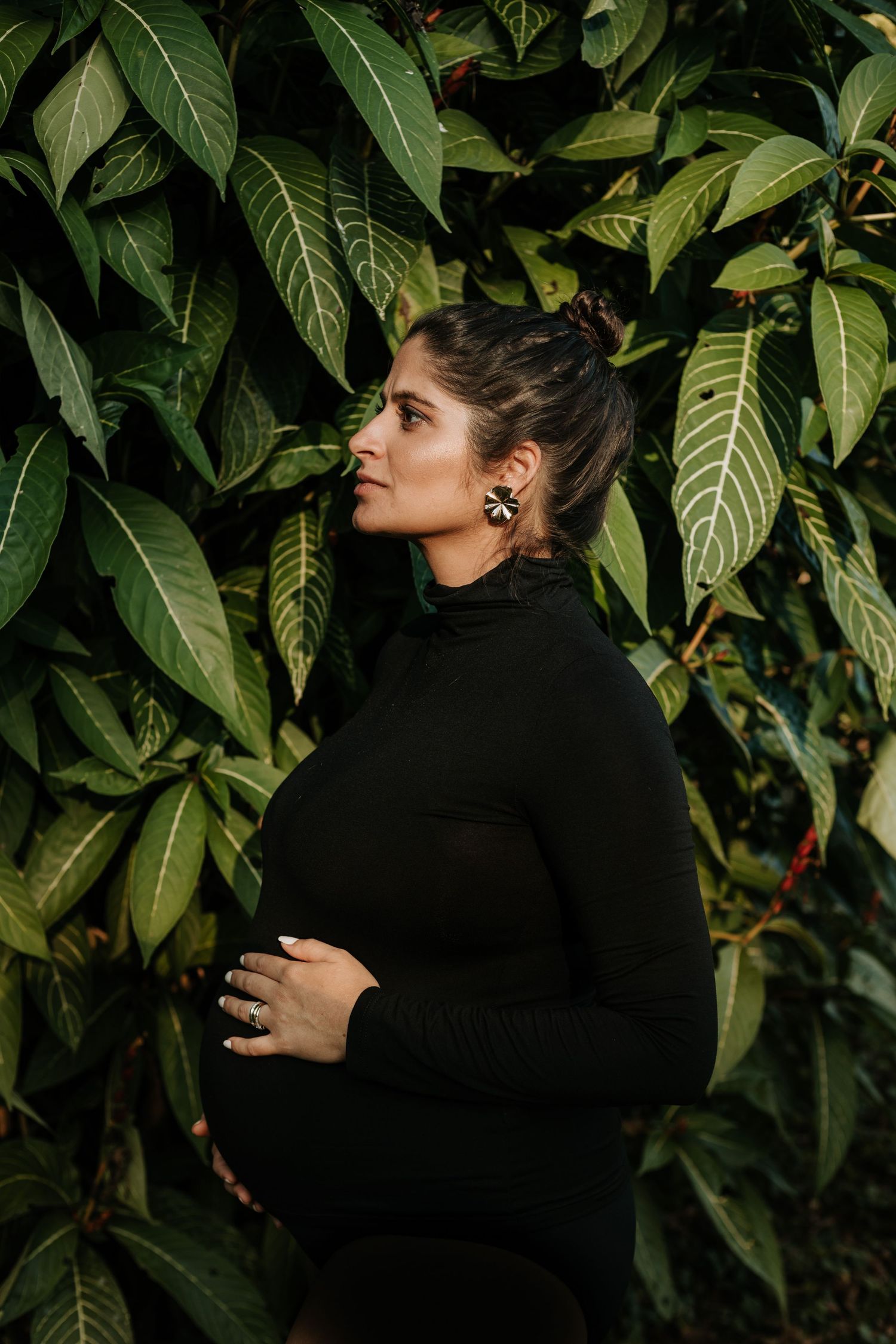 A person in a black sweater stands against a backdrop of lush green leaves in a dynamic fashion sequence.