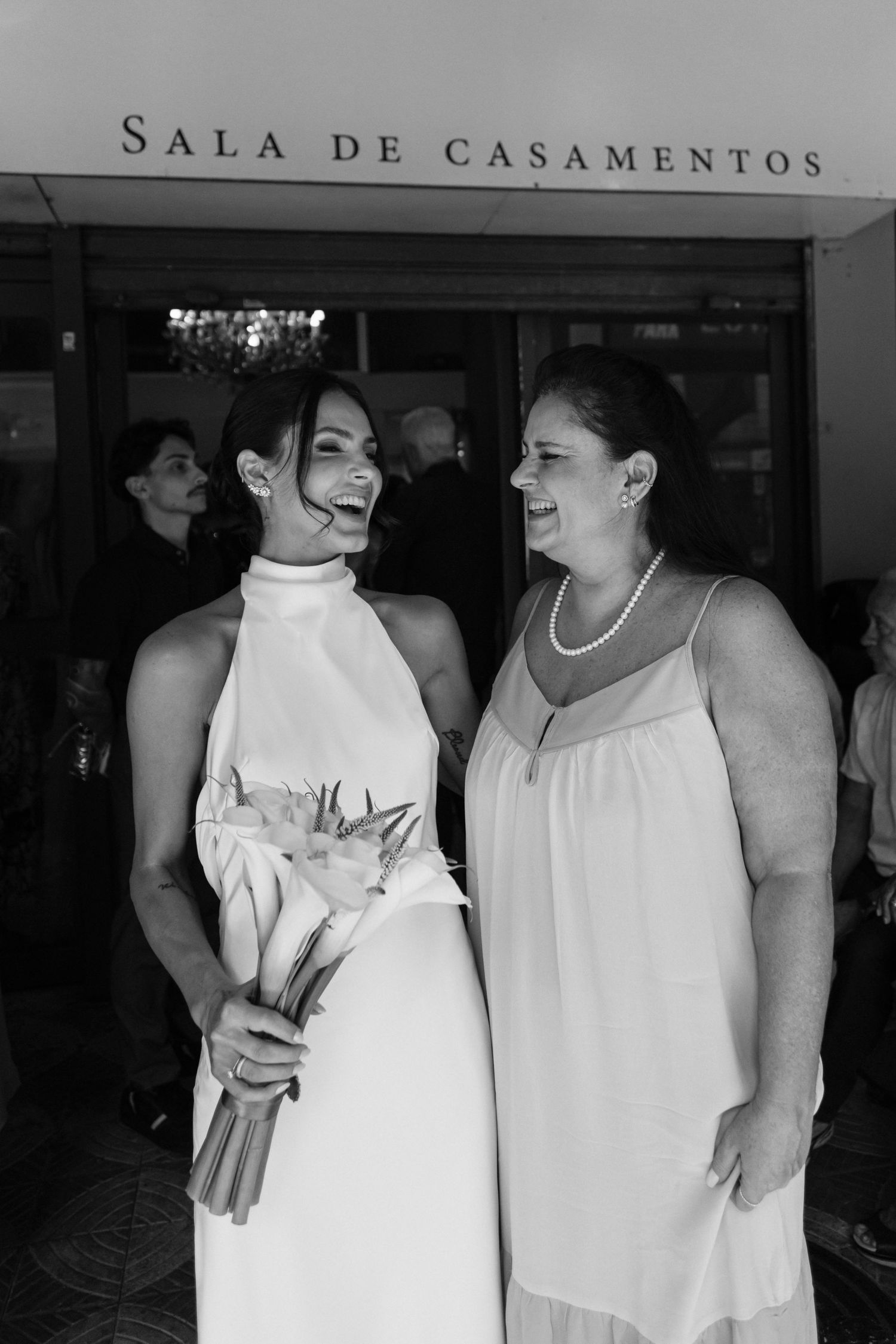 Two people share joyful laughter outside wedding venue entrance.