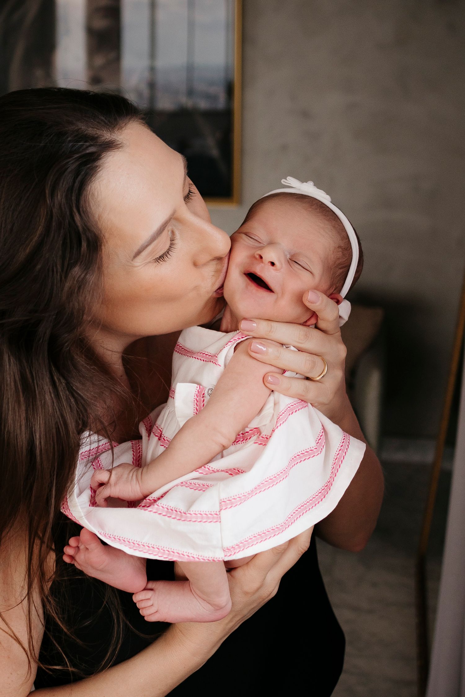 Intimate moment of parent giving newborn in pink dress a gentle kiss.