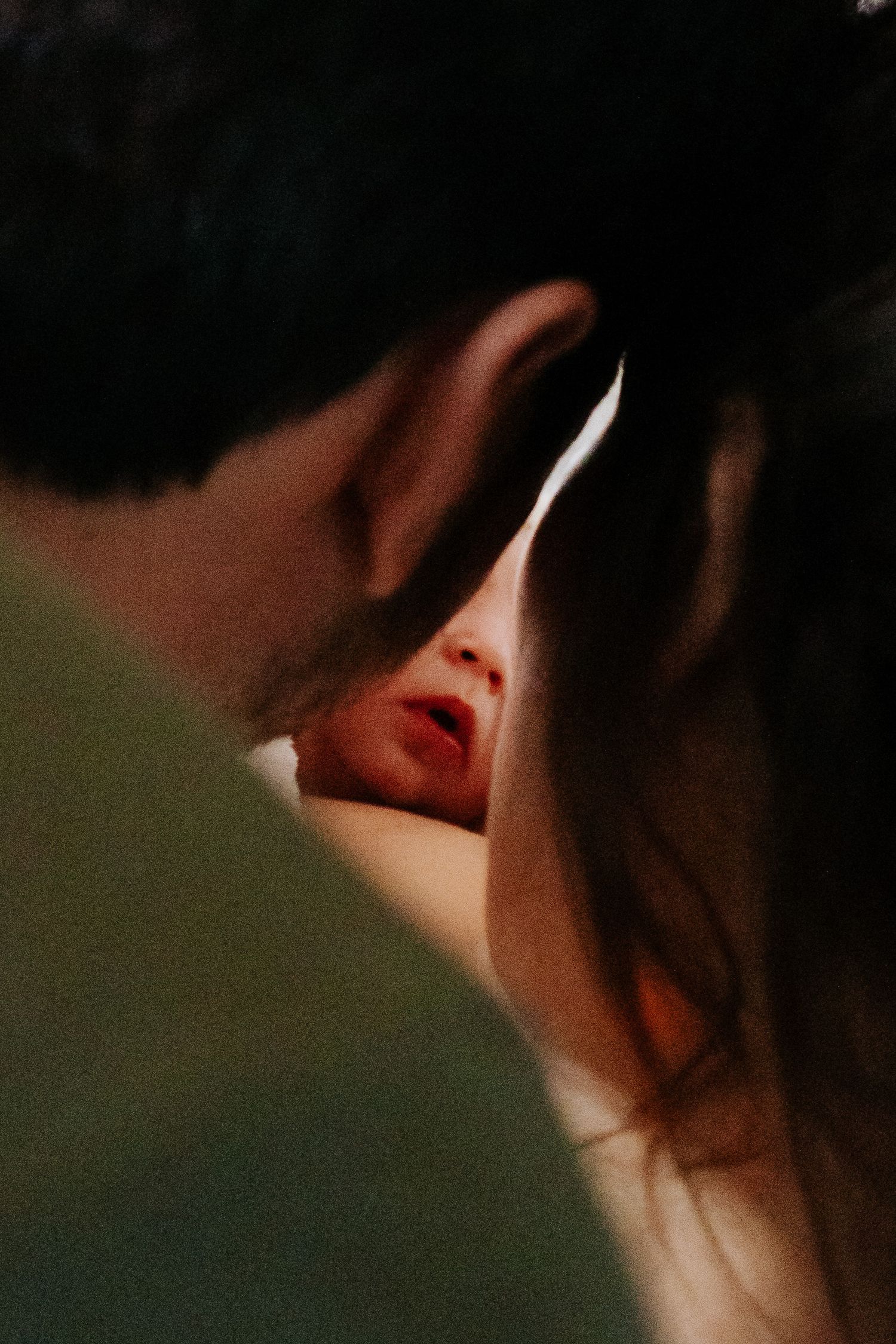 Two people in an intimate close-up moment, faces nearly touching in soft, moody lighting.