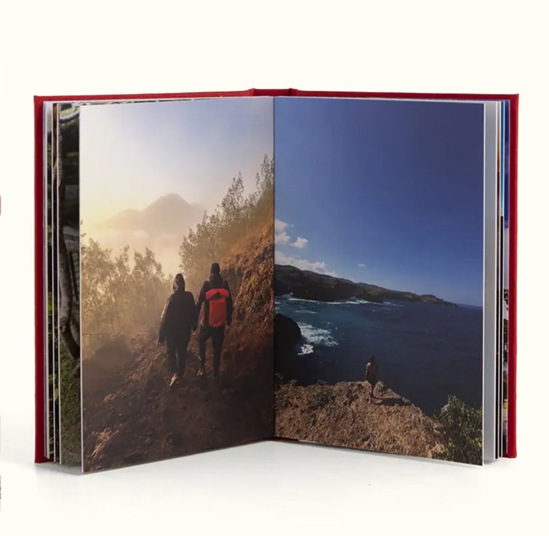 Open hardcover photo book displaying two scenic outdoor adventure photos of hikers on rocky cliffs and coastal ocean views.