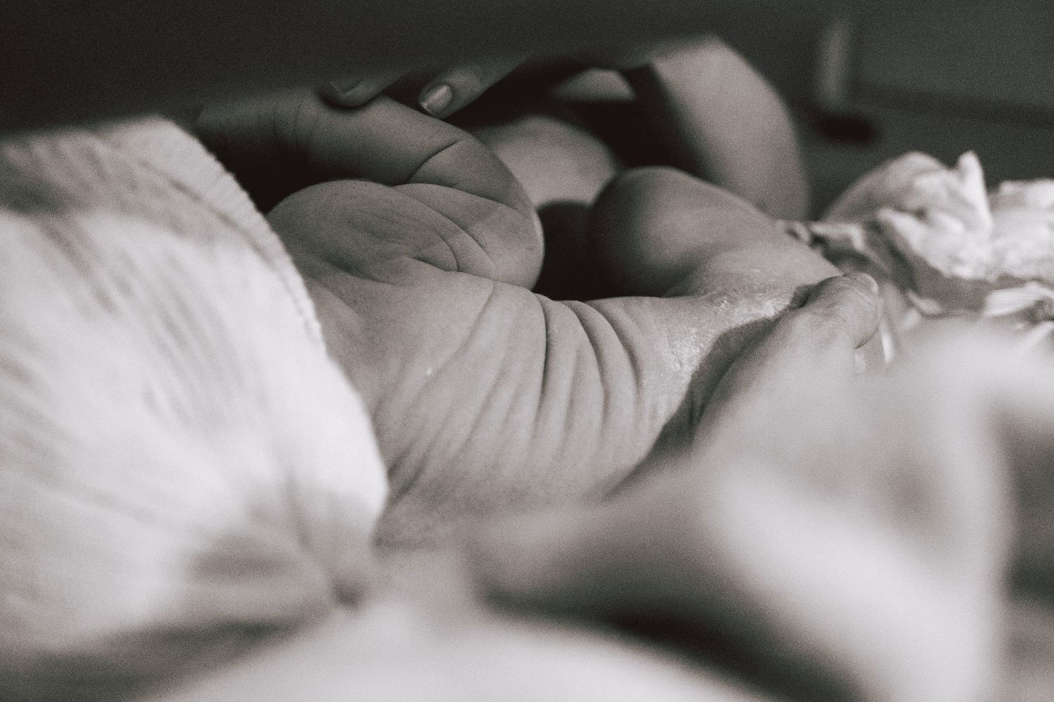 Close-up black and white photo of a person resting peacefully in soft white rumpled bed sheets.