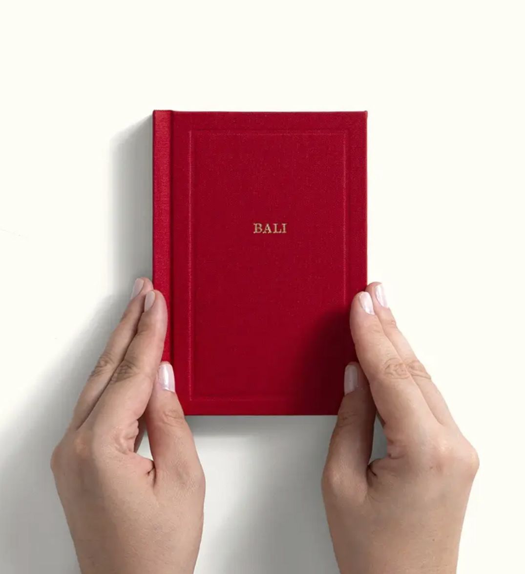 Hands holding a small red hardcover Bali journal book with gold embossed text.