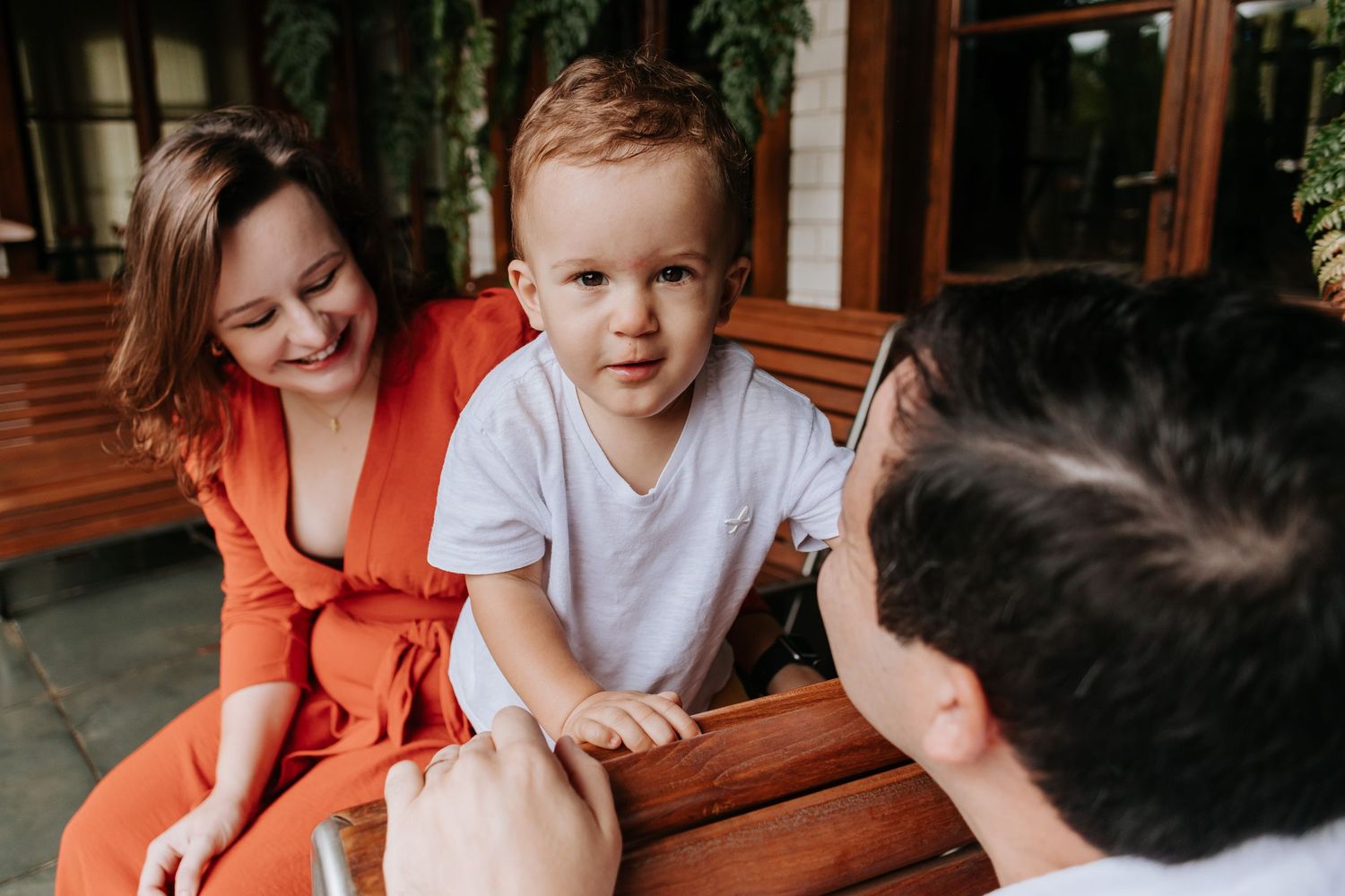 A candid family moment captured on a wooden bench outdoors with natural lighting.