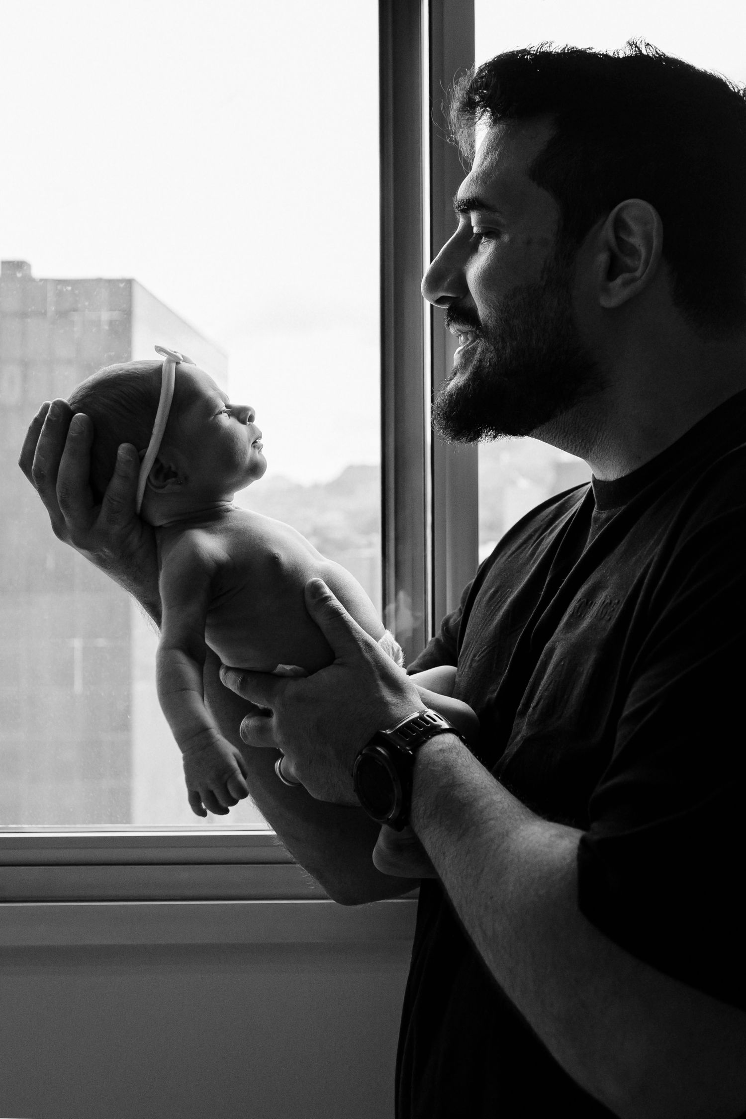 Black and white photo of a tender moment between parent and newborn by a window.