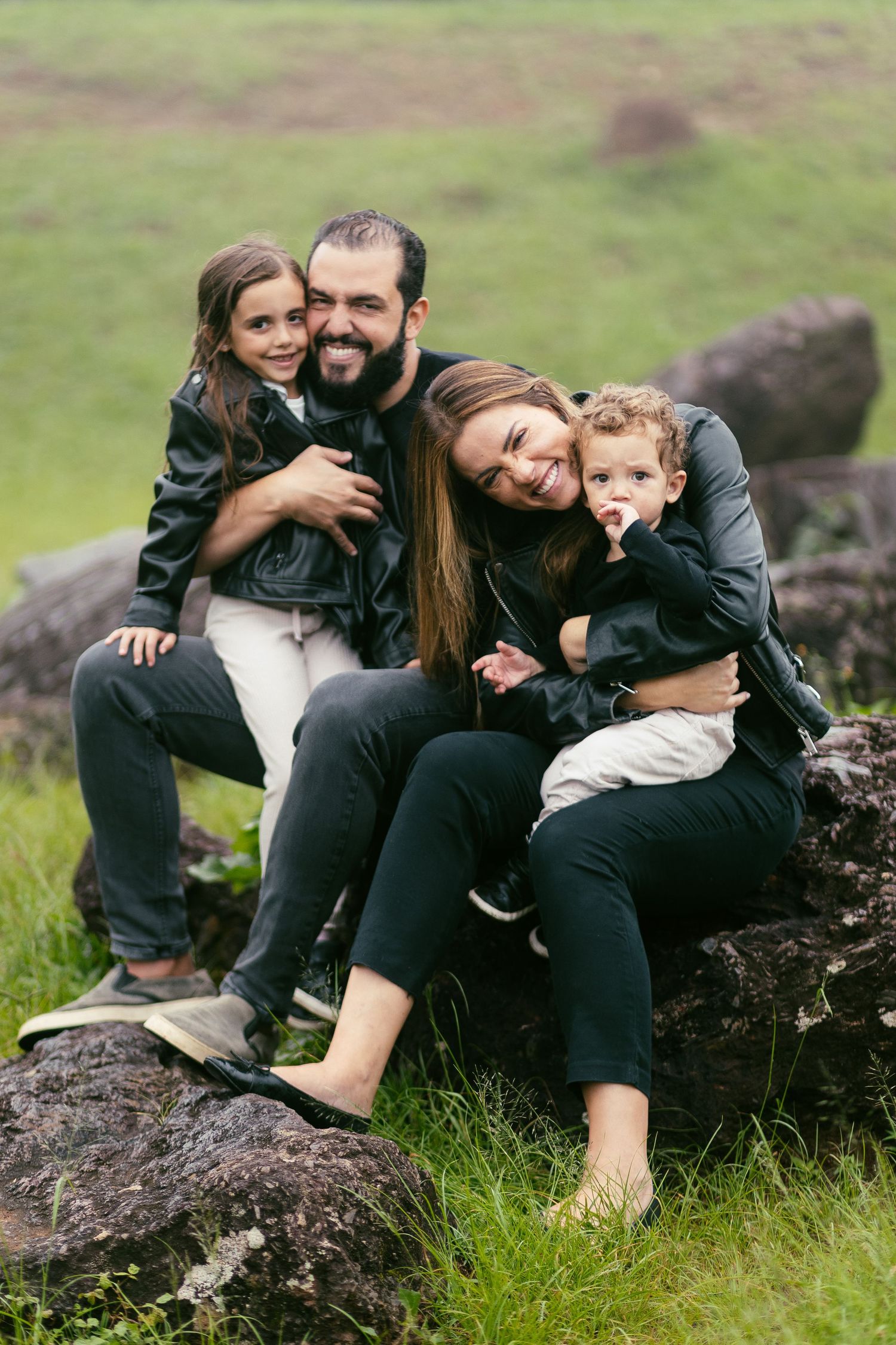 A family in matching dark outfits sits together on rocky terrain surrounded by green grass.