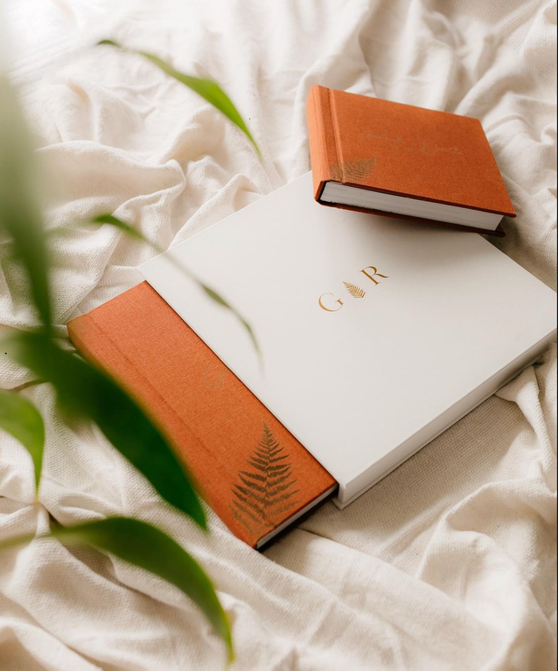 Elegant white and terracotta wedding guest book with gold monogram GR and fern detail on cream fabric.