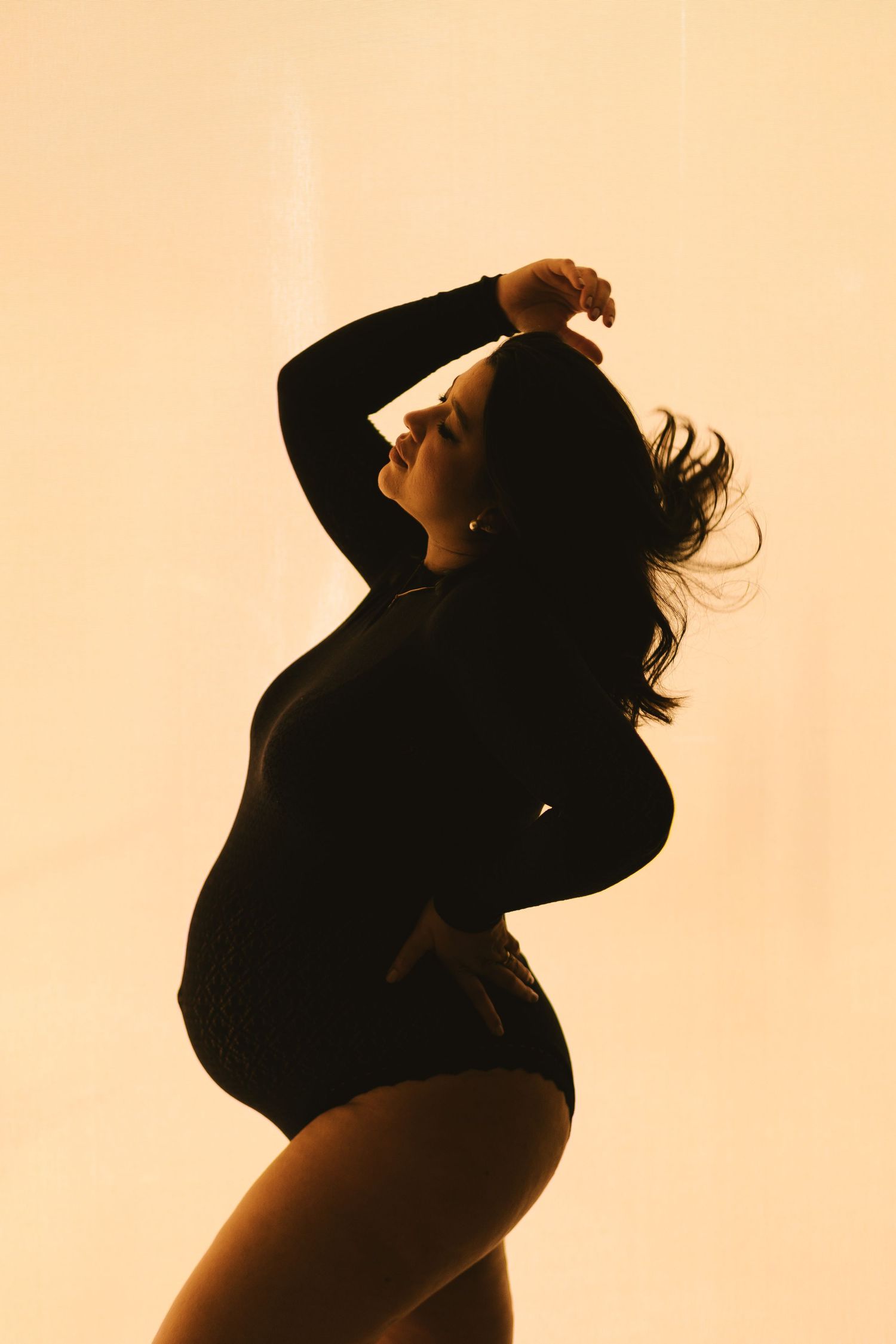 Silhouette of a woman in a bodysuit posing gracefully against a warm golden backlit background.