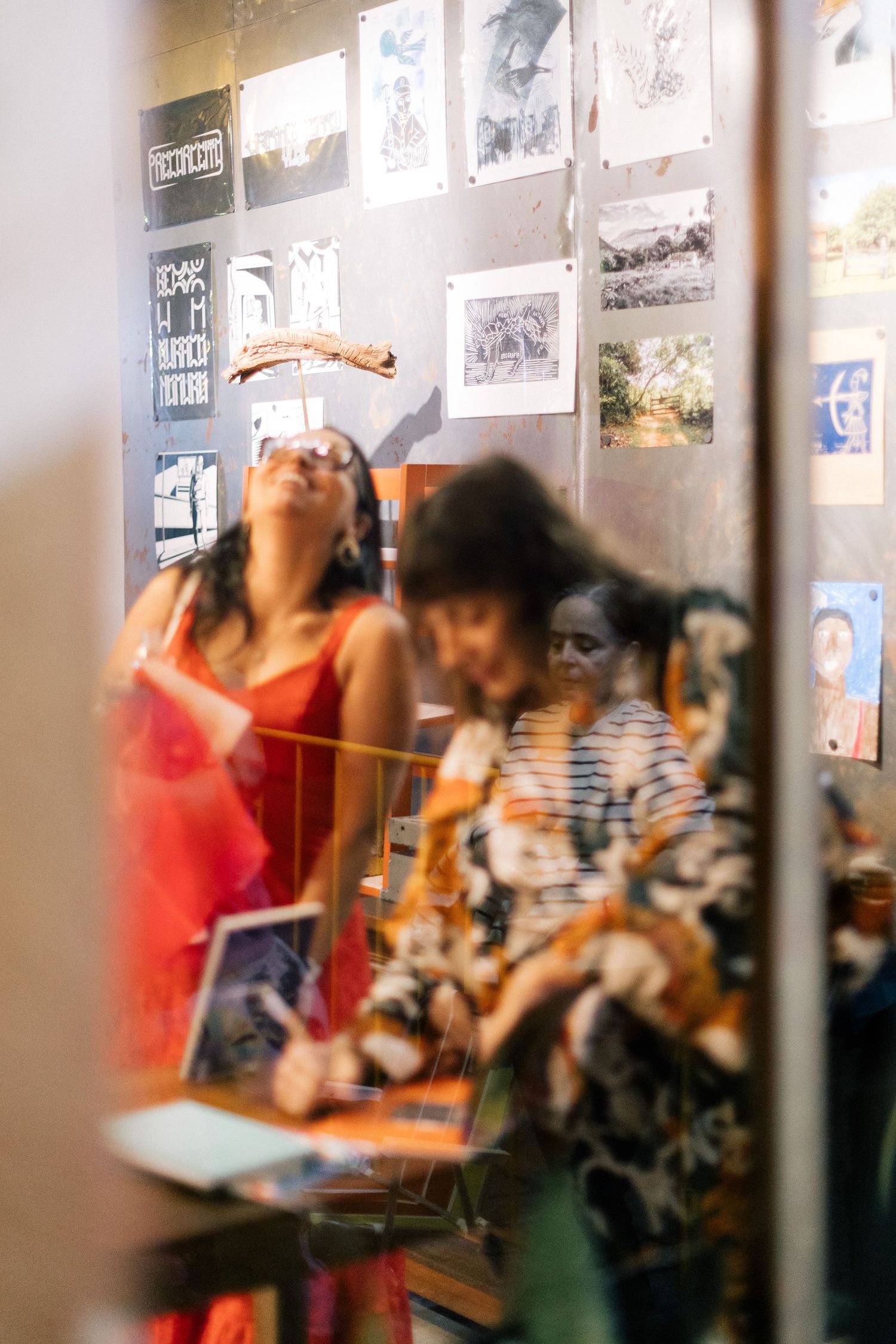 Women viewing art exhibition with photos and drawings displayed on gallery walls in a warm, softly lit space.