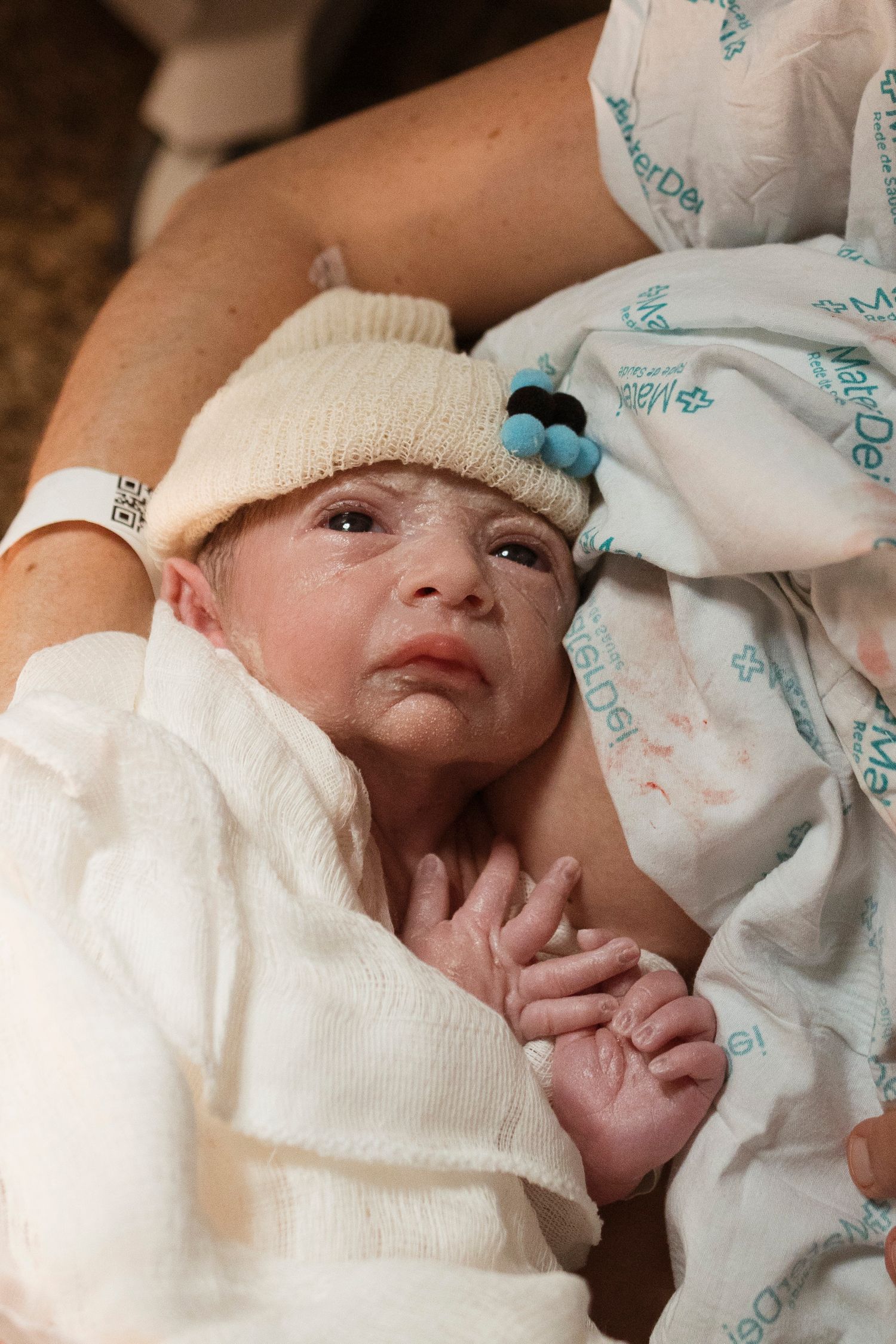 Newborn wearing a white knit cap and hospital gown.