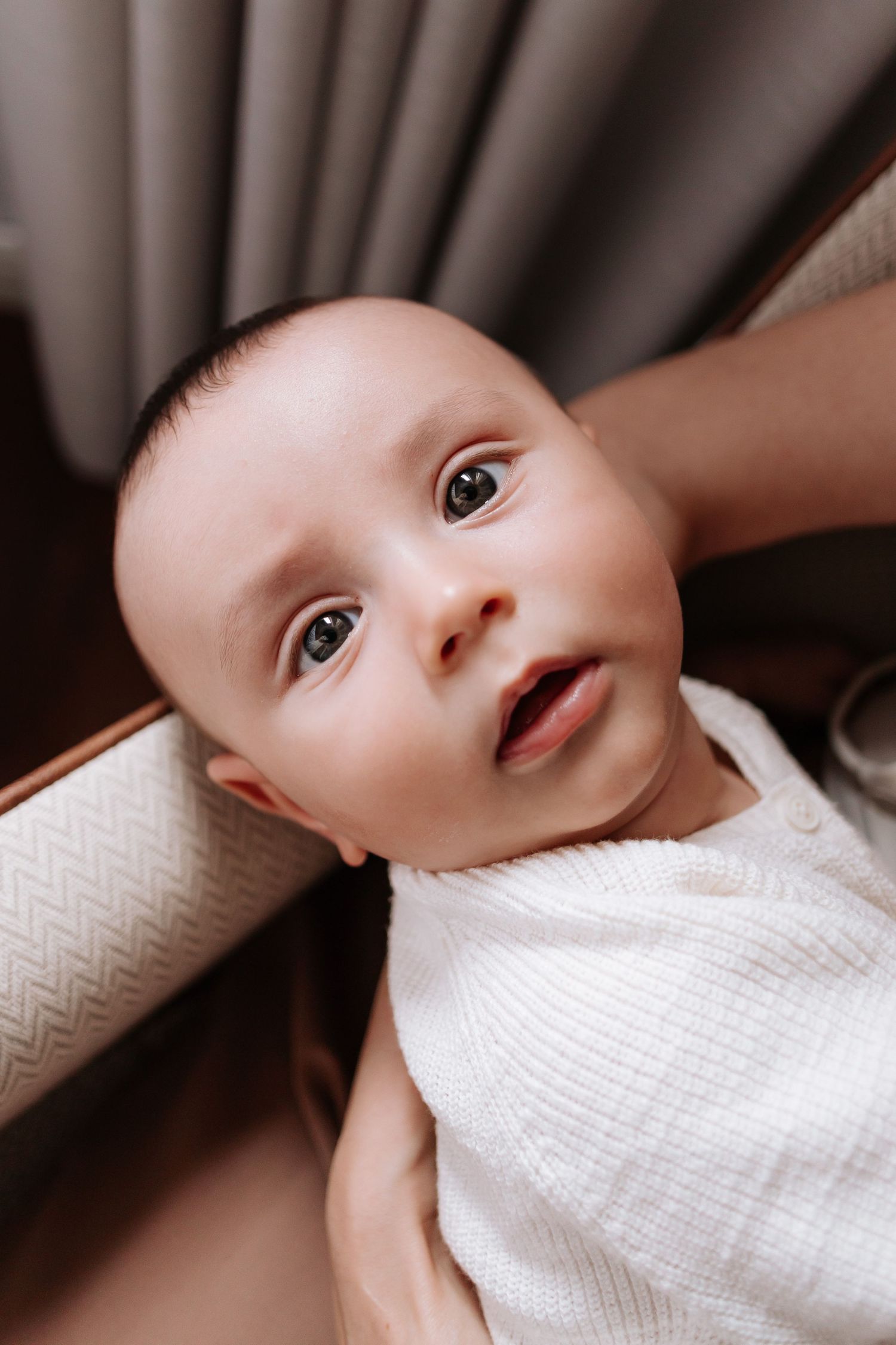 A baby wearing white clothing looks up with a gentle expression in a series of connected close-up photos.