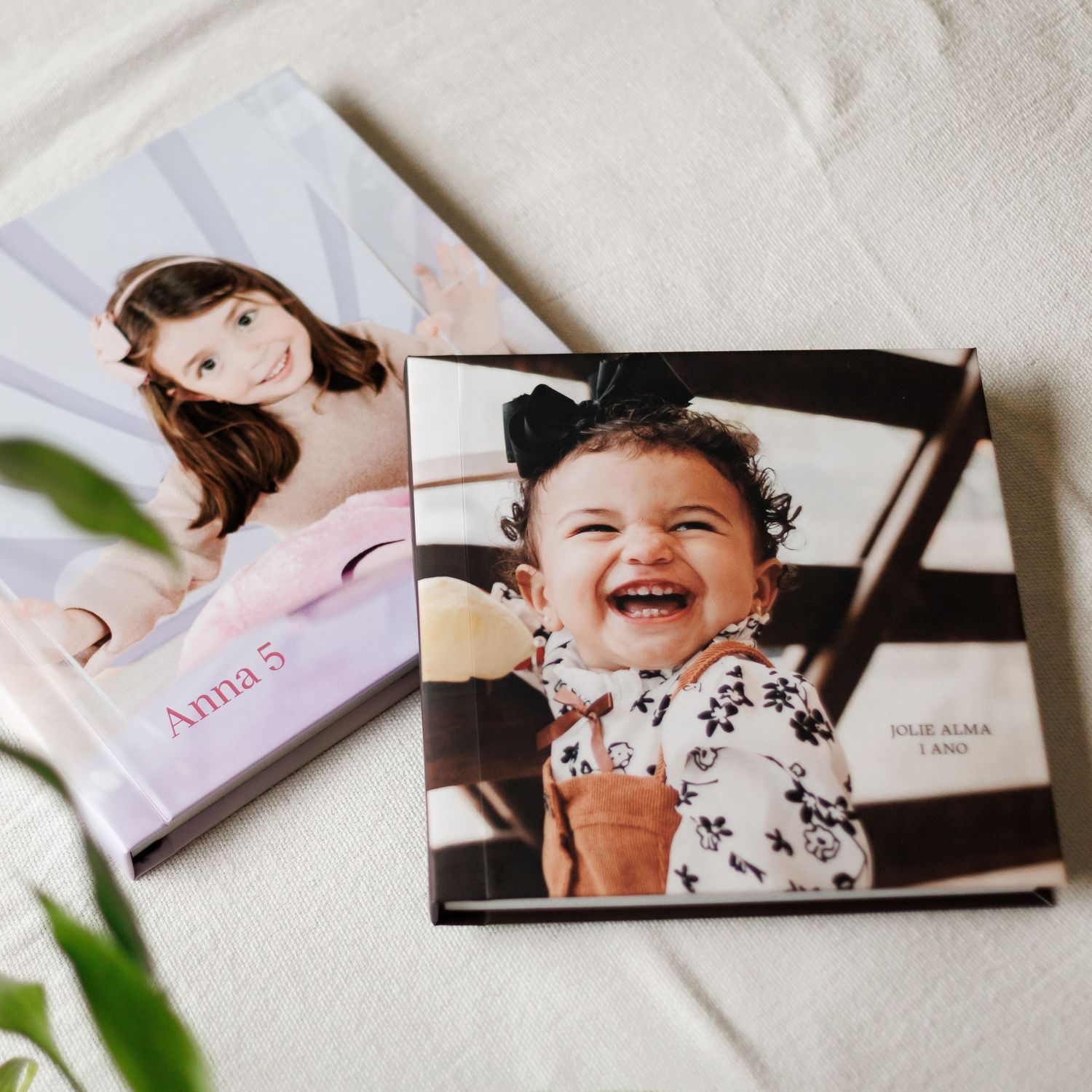 Two personalized photo books featuring children, one showing a girl named Anna at age 5, another with a laughing baby in a floral outfit.