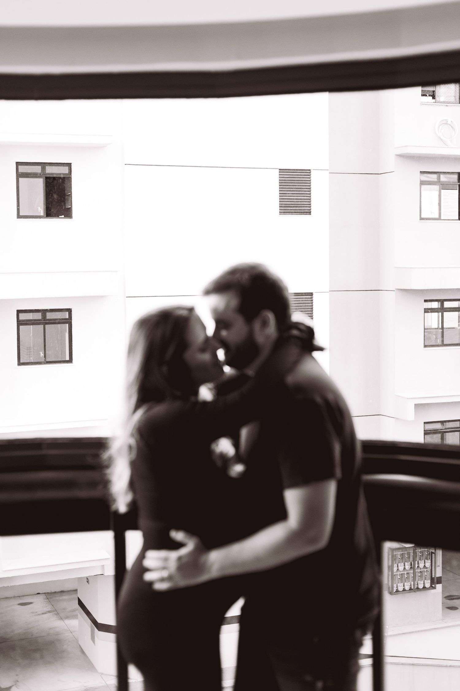 Black and white photo of loving couple embracing and kissing on urban balcony.