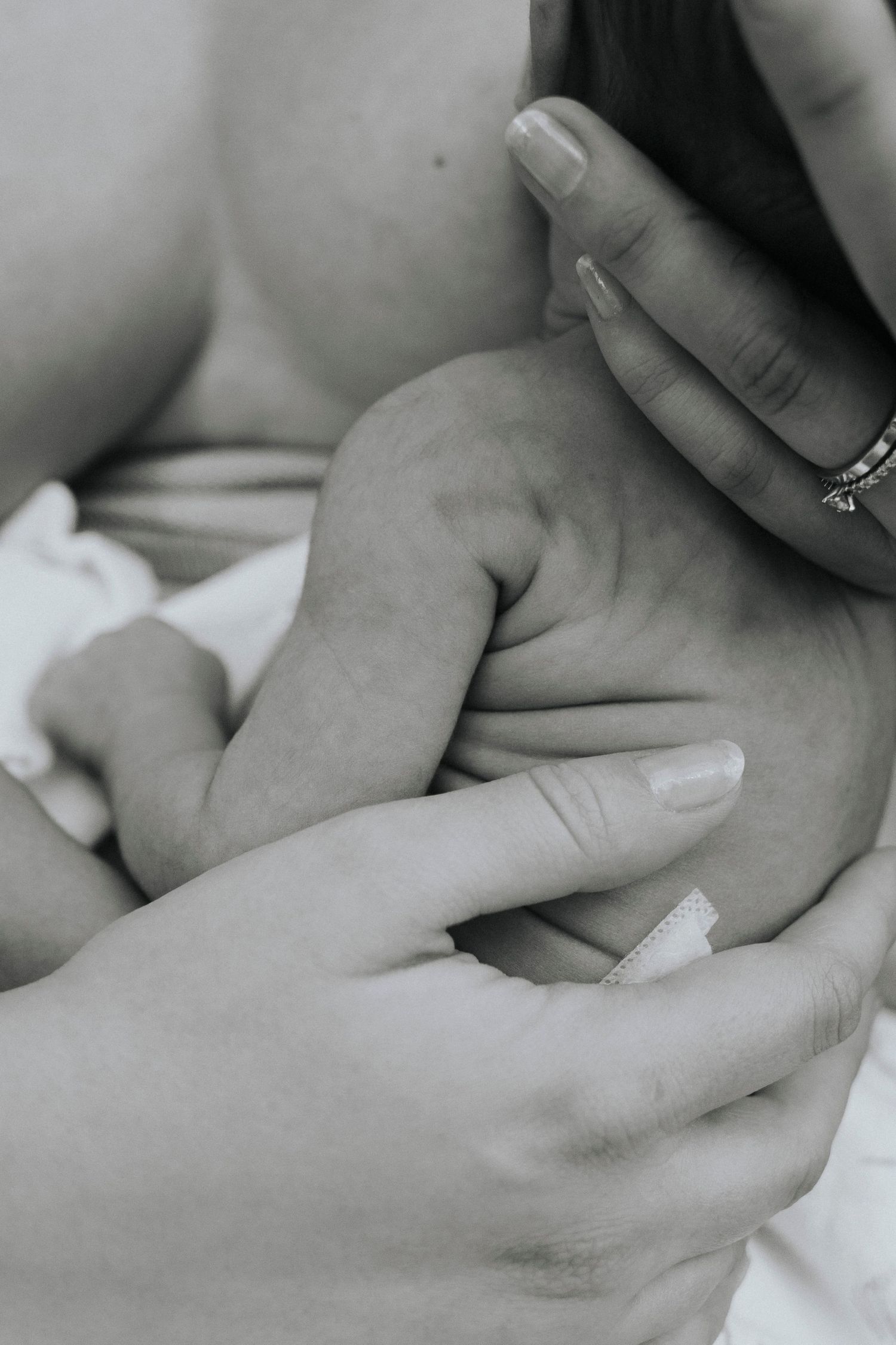 Gentle hands cradling infant's tiny arm in black and white photograph.