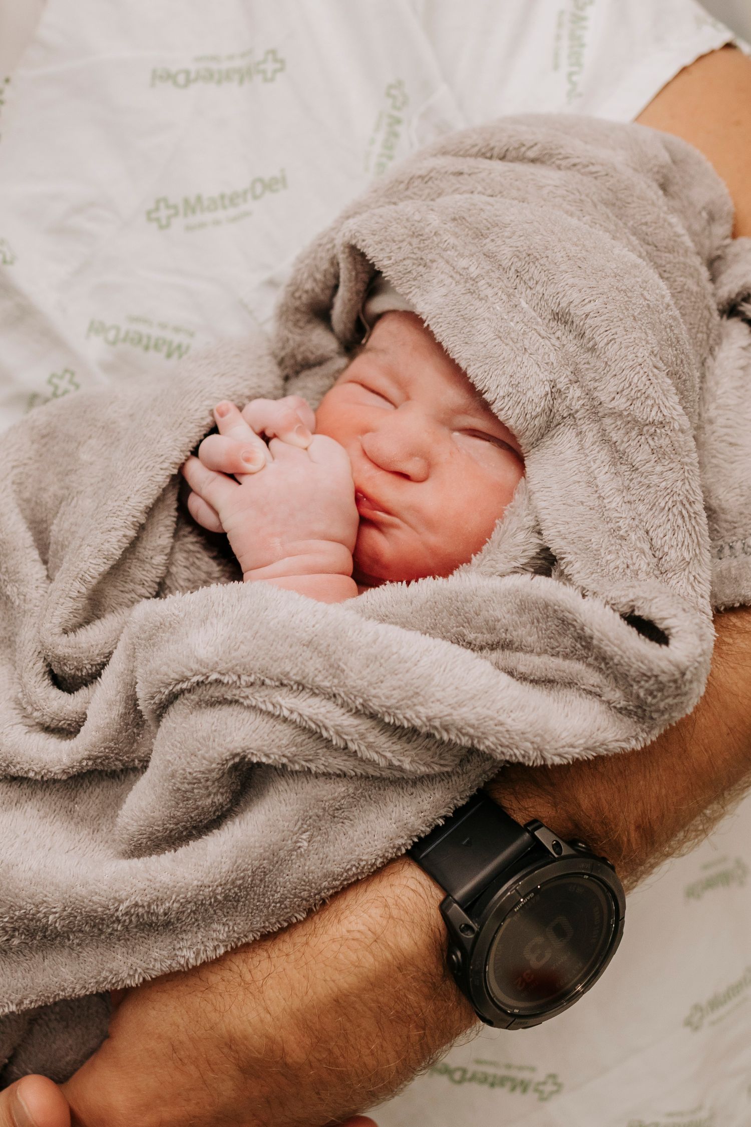 Newborn baby wrapped in soft grey blanket sleeping peacefully.