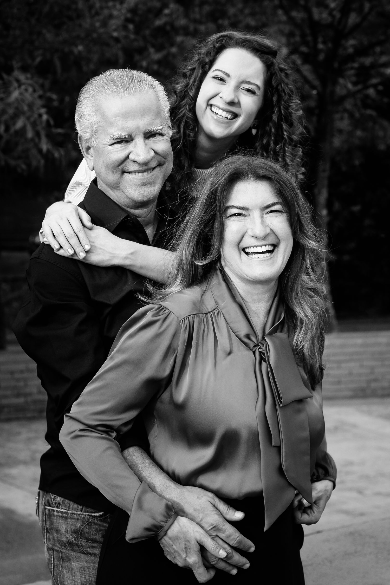 A cheerful black and white portrait of three people sharing laughter and hugs outdoors.