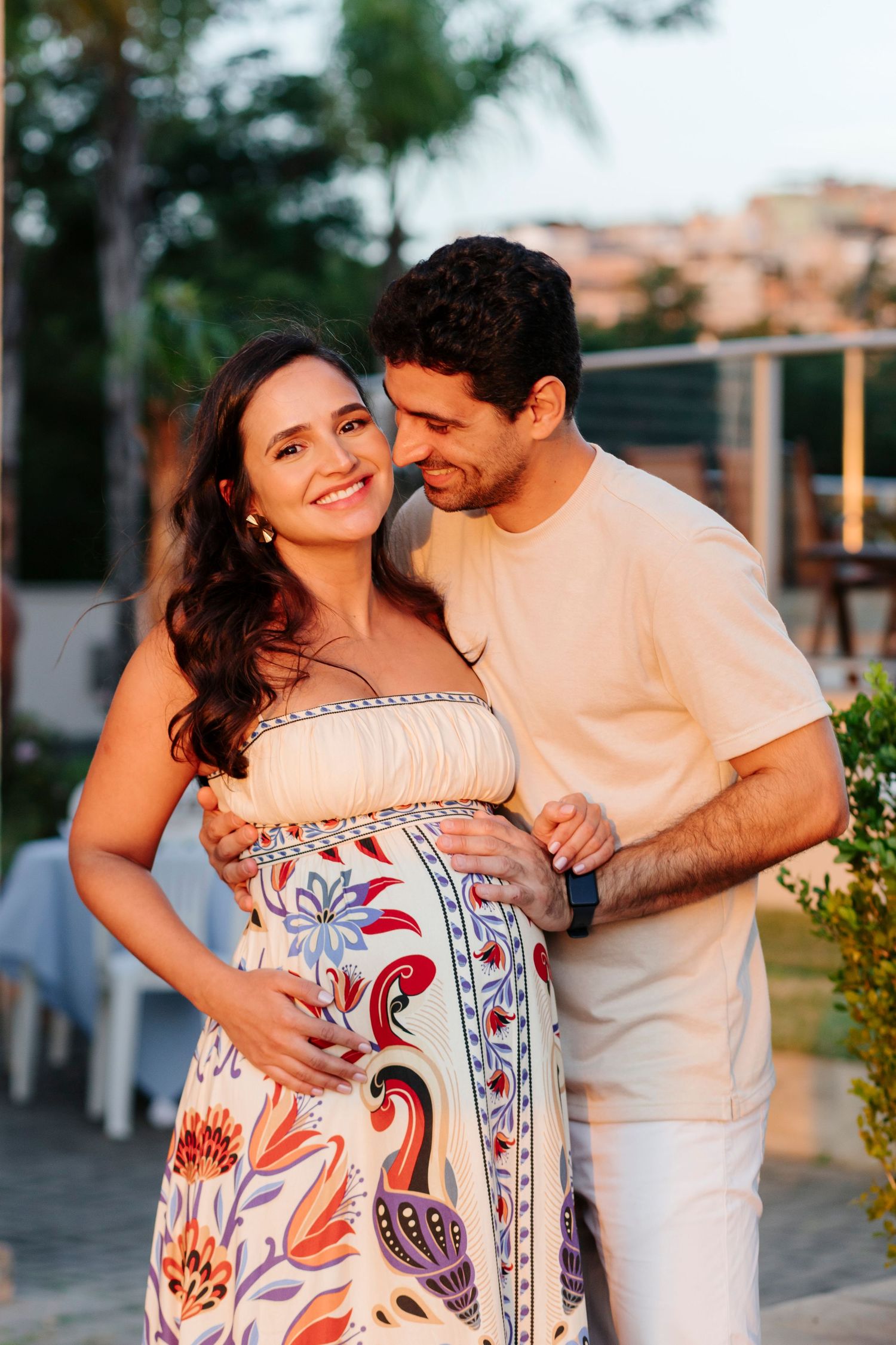 A couple in white and floral outfits share intimate moments in an outdoor setting during sunset.