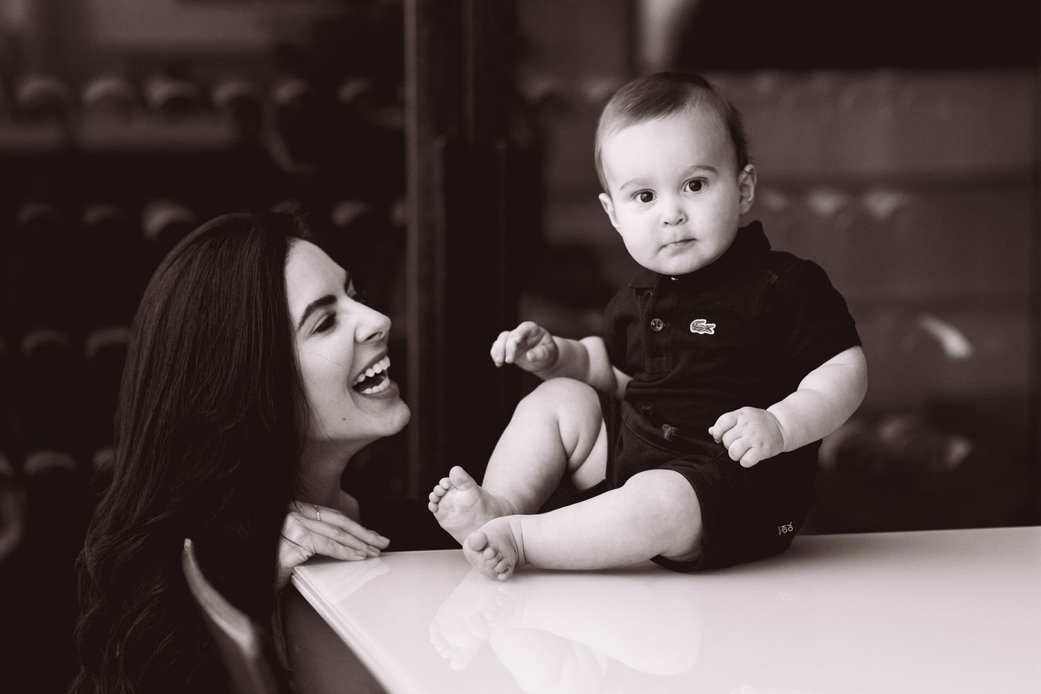 Black and white photo of a smiling mother holding her happy baby on a reflective surface.