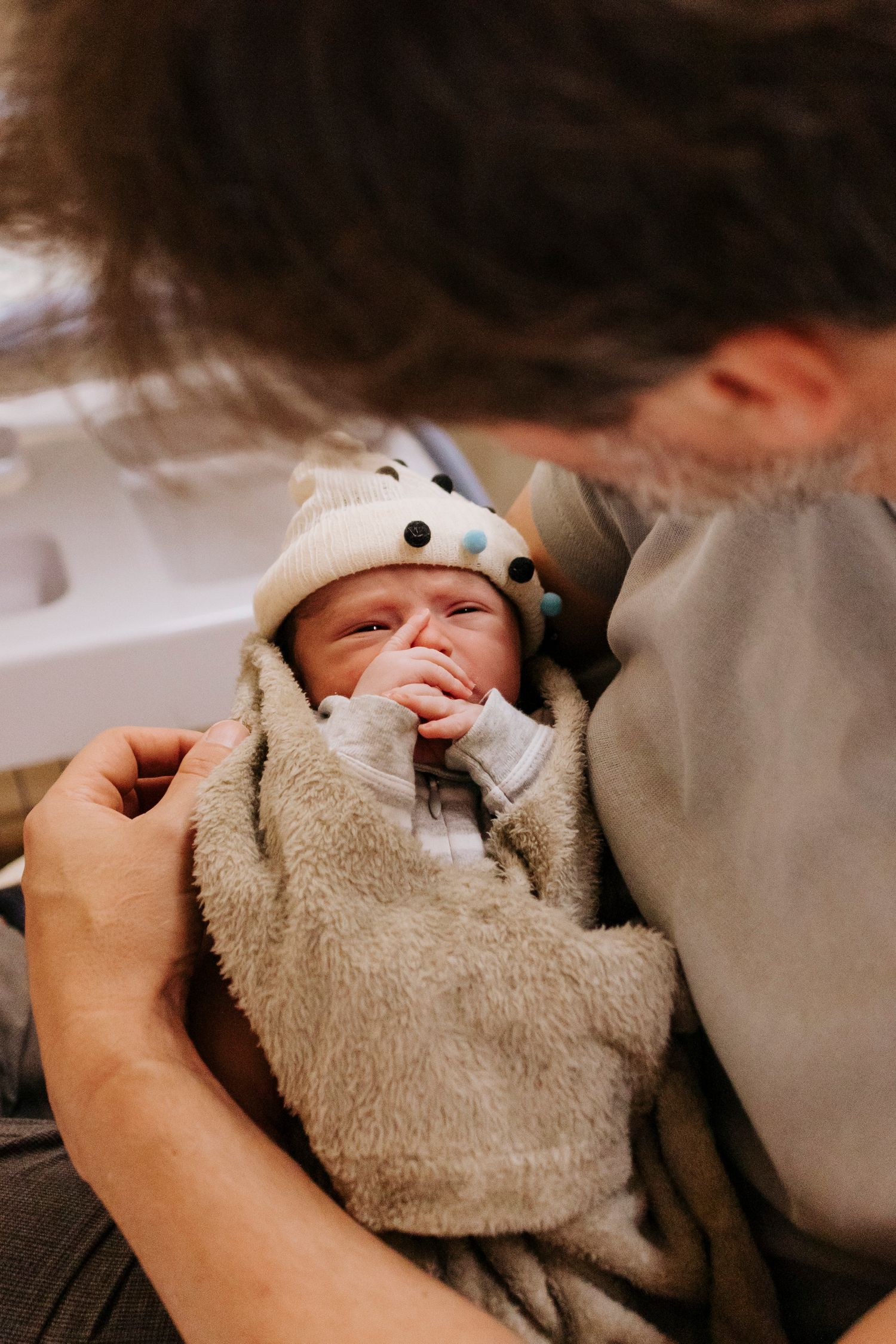 A newborn baby wrapped in a plush grey blanket wearing a cute animal-themed hat.