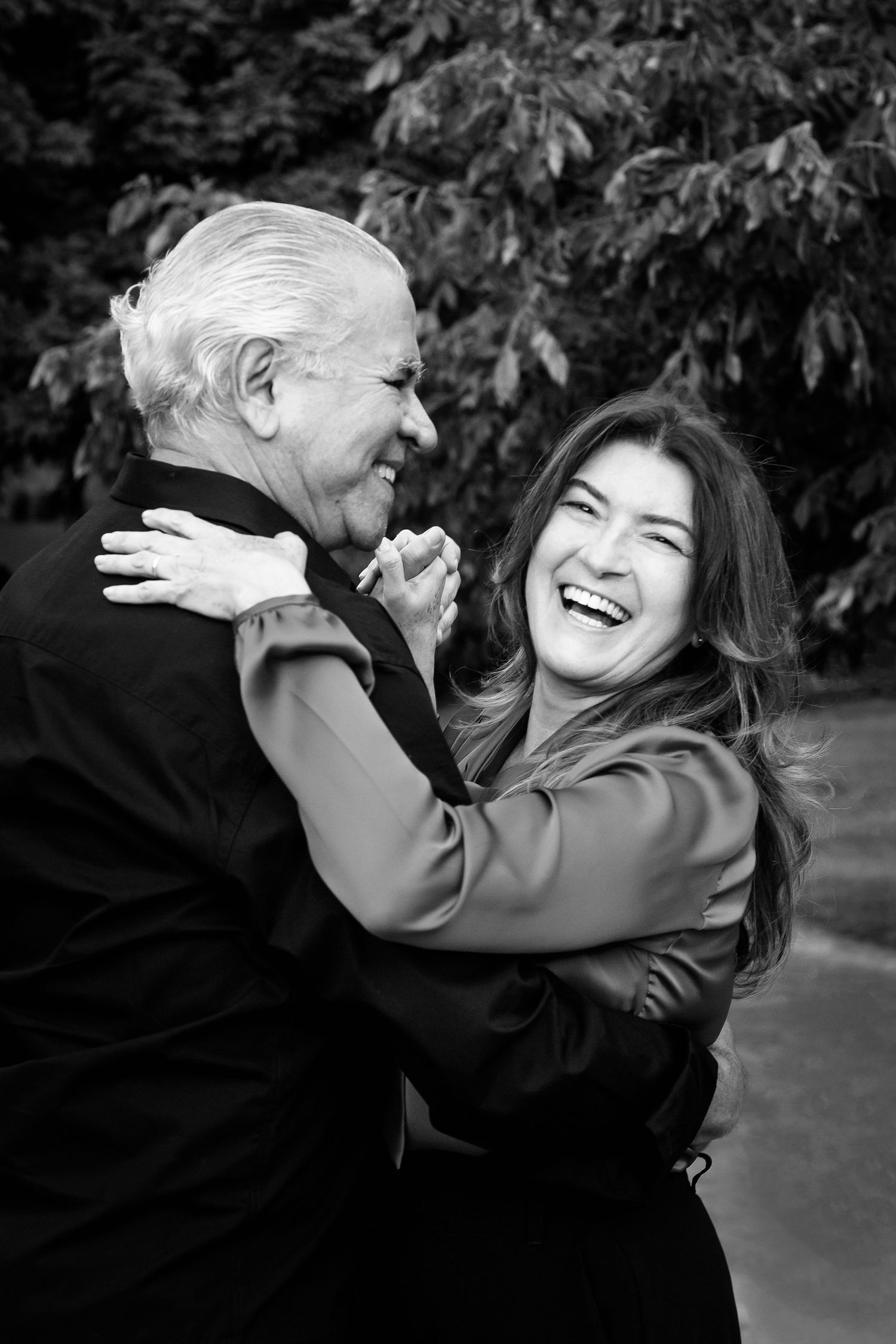 A joyful black and white portrait capturing a laughing embrace between two people outdoors.