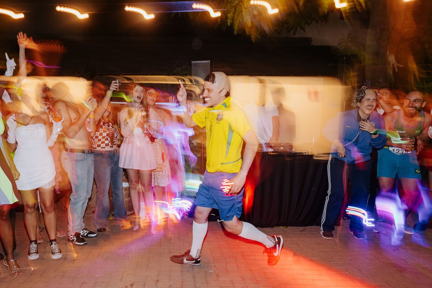 Dancer performs energetic breakdance move on illuminated dance floor while crowd watches at nighttime party.