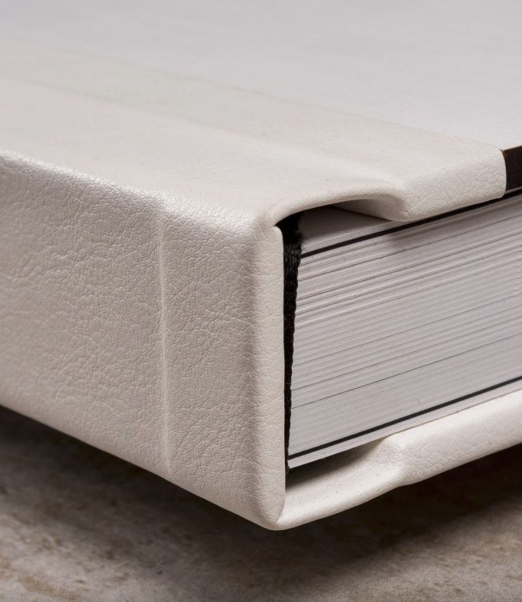 Close-up of a white leather-bound book with thick pages, showcasing elegant craftsmanship and textured cover detail.