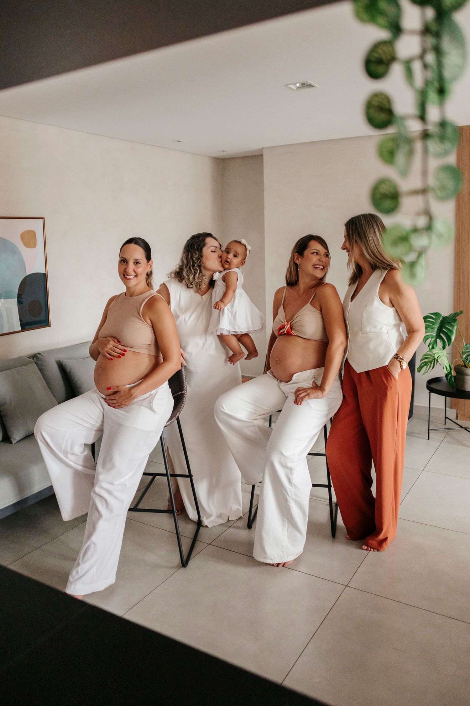 Group in elegant beige and terracotta dresses poses for fun candid photos in a bright white studio space.