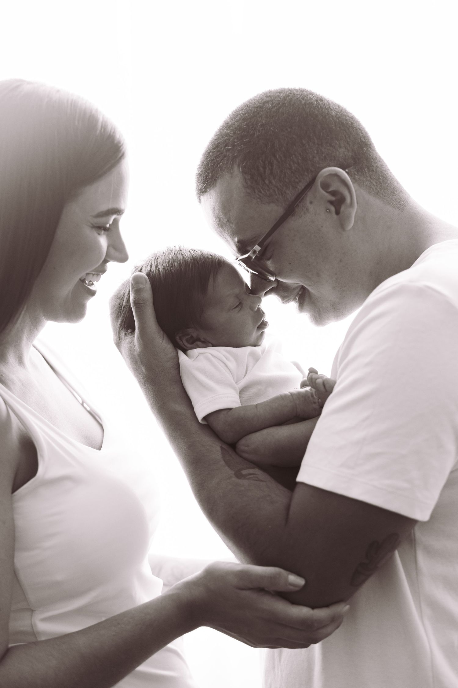 Black and white photo of smiling parents holding their newborn baby close, sharing a tender family moment.