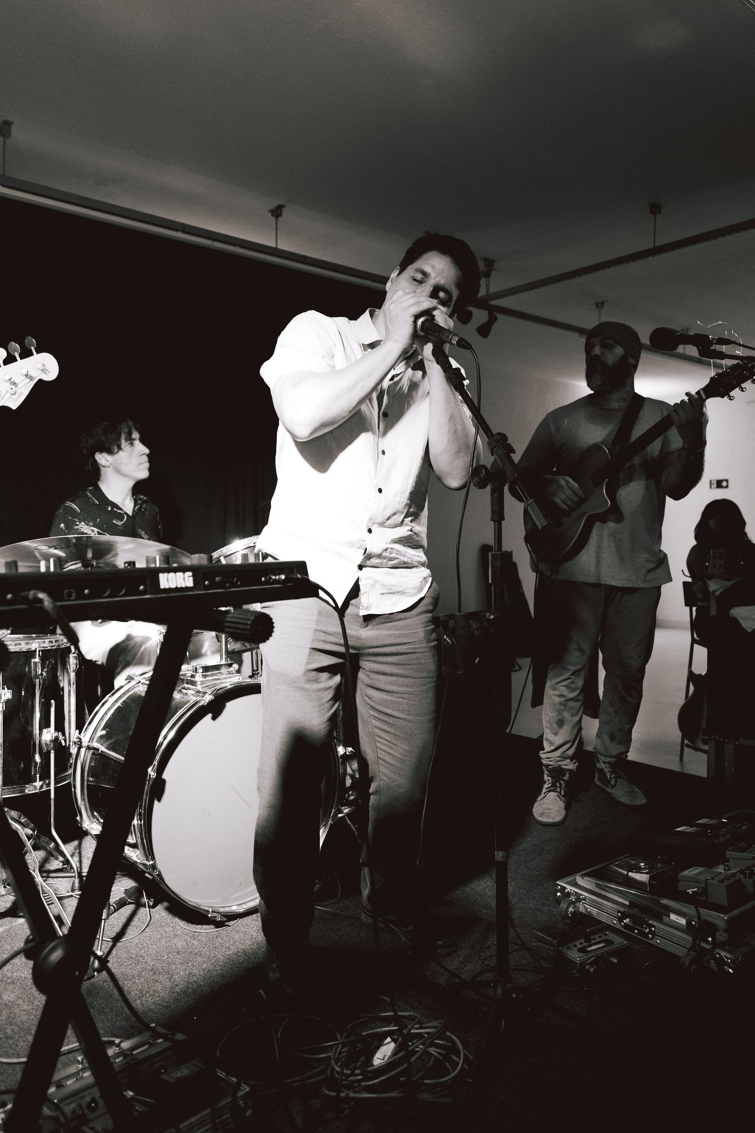 Black and white photo of a band performing in a small venue with keyboard, bass guitar and vocals on stage.
