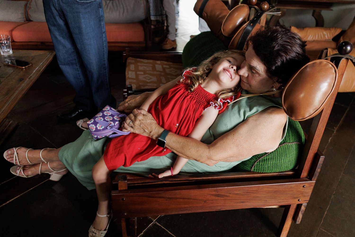 Two people share an intimate moment while lying on wooden benches in a dimly lit setting.