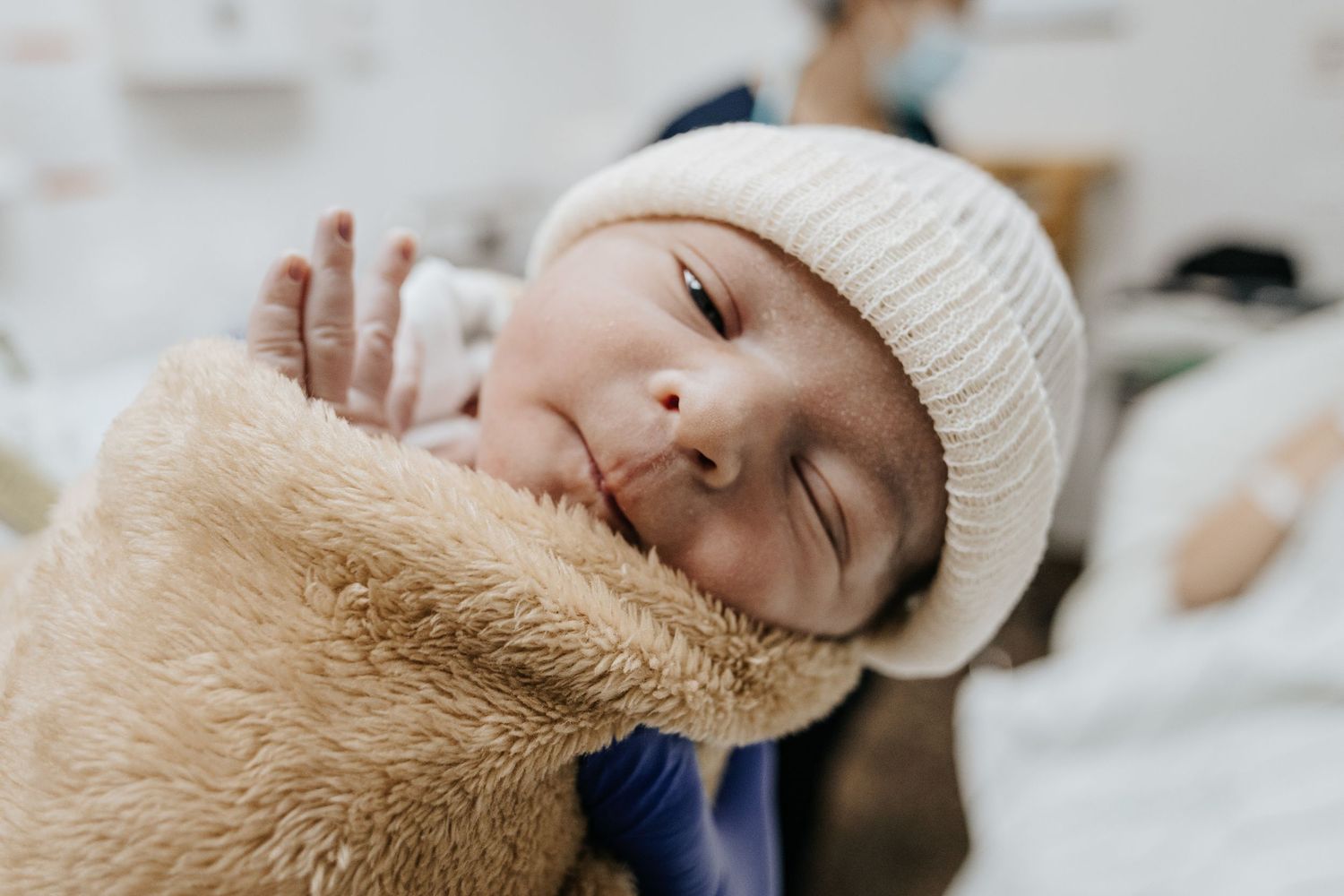 Peaceful newborn wearing knit hat while swaddled in plush beige blanket.