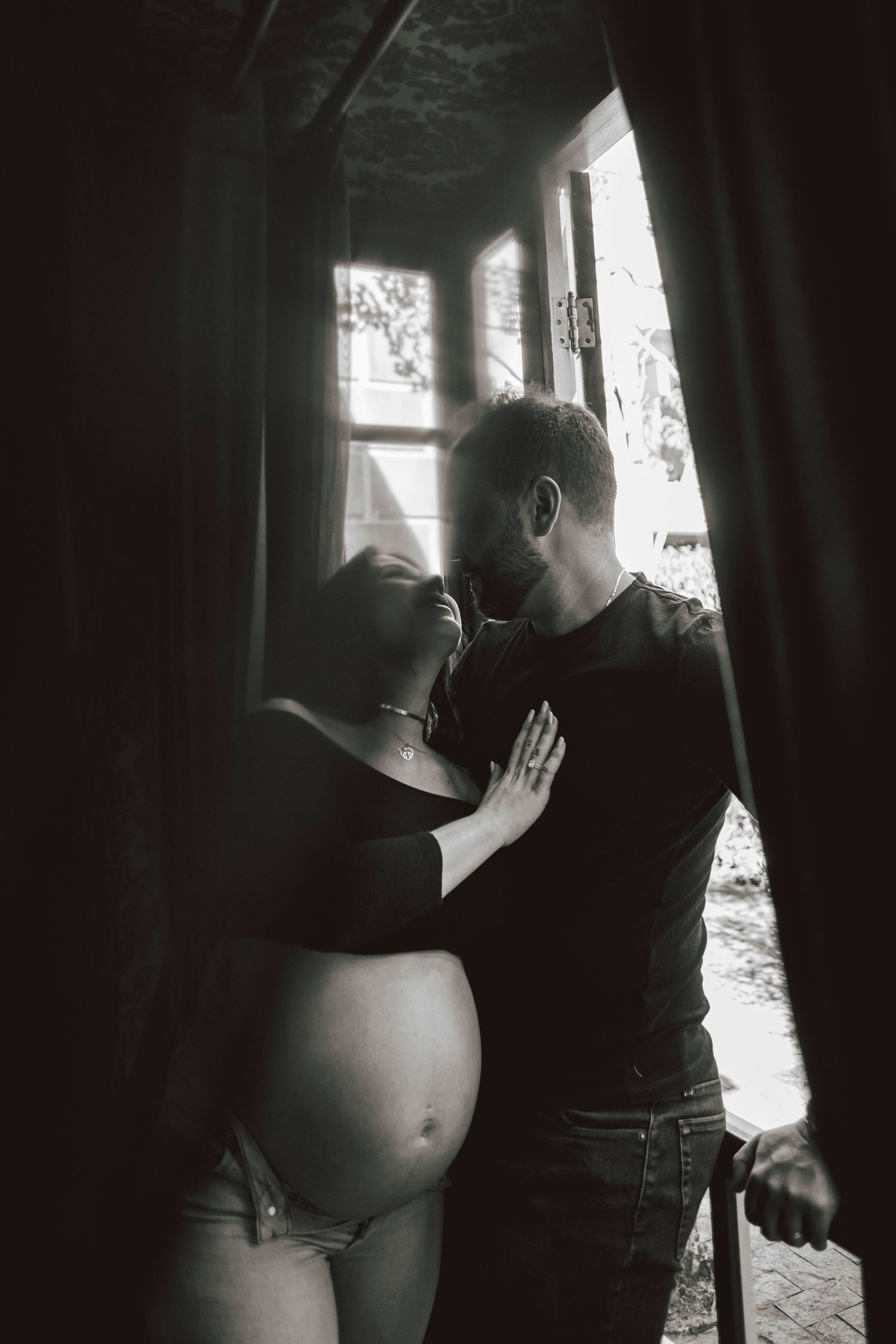 Black and white intimate portrait of expecting couple in window light.