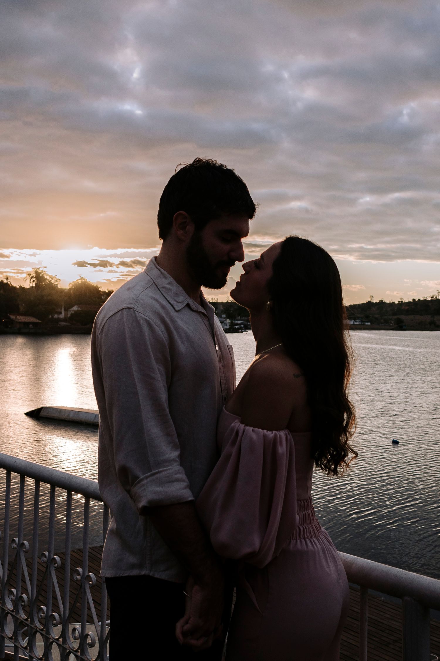 Romantic silhouette of couple embracing by lake during sunset.