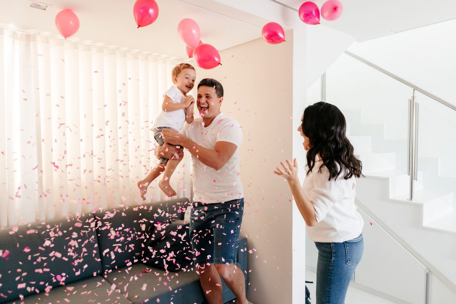 A couple celebrates with pink balloons and confetti during a joyful indoor photoshoot.