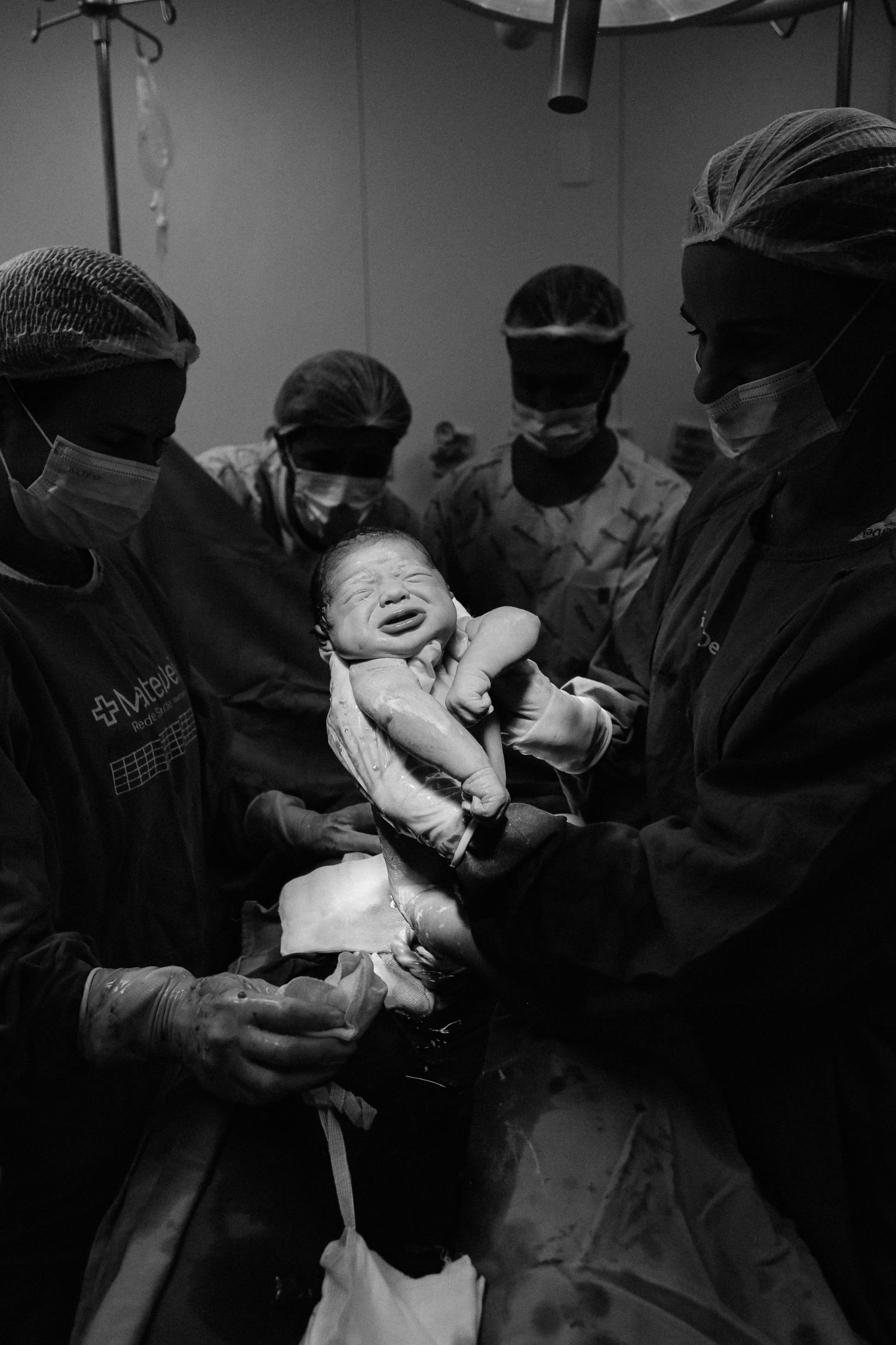 Medical team in surgical gear holding newborn baby in delivery room.