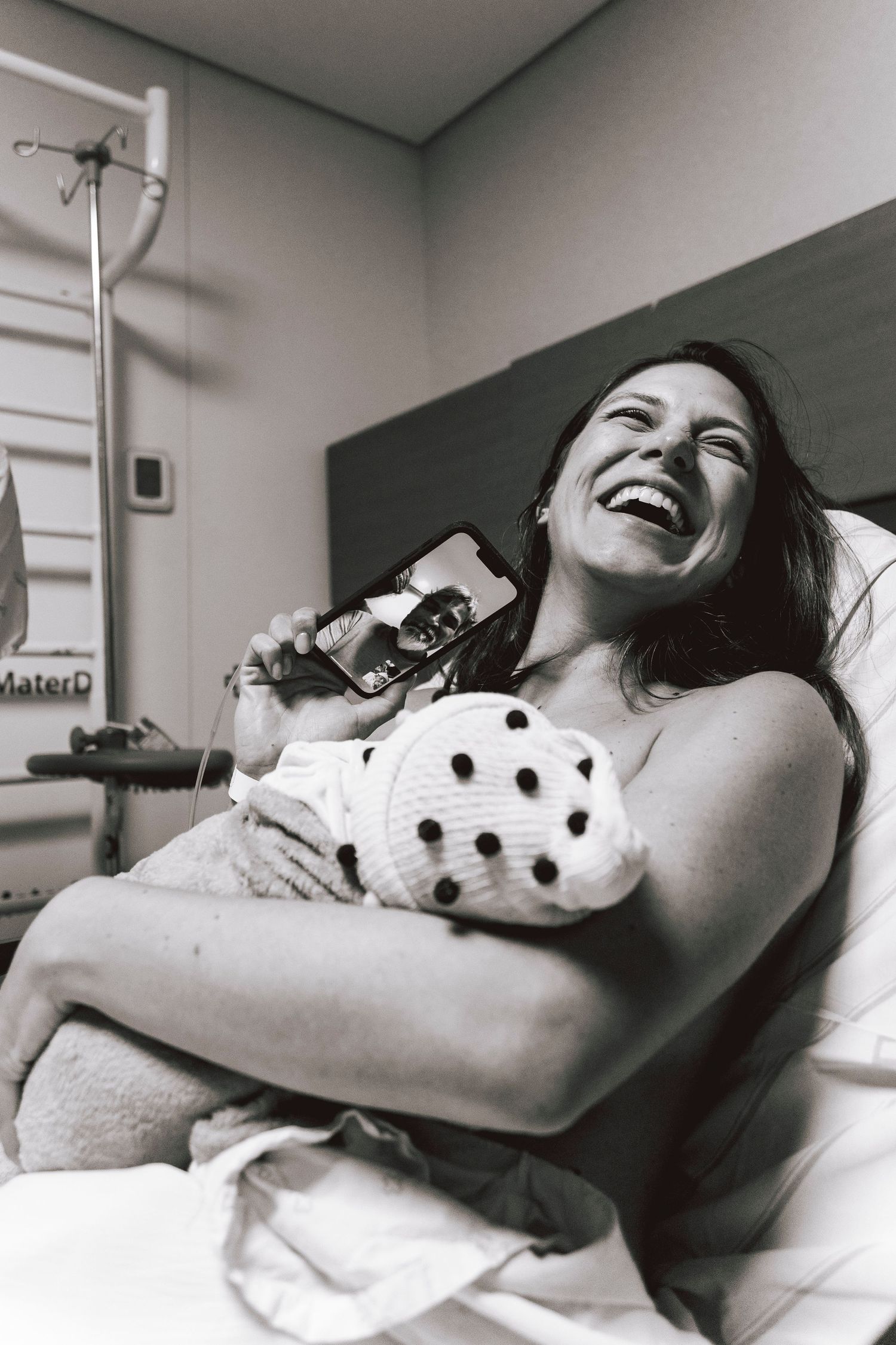 Joyful moment captured in black and white as new mother holds baby in hospital room.