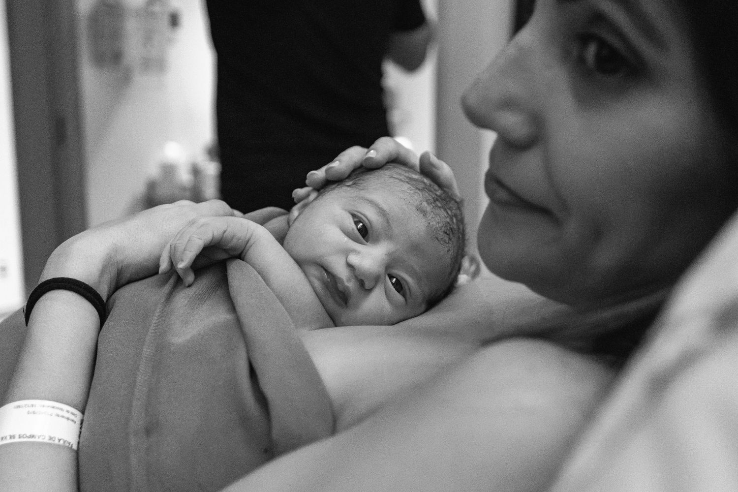 A tender moment captured as a newborn rests against soft fabric in black and white.