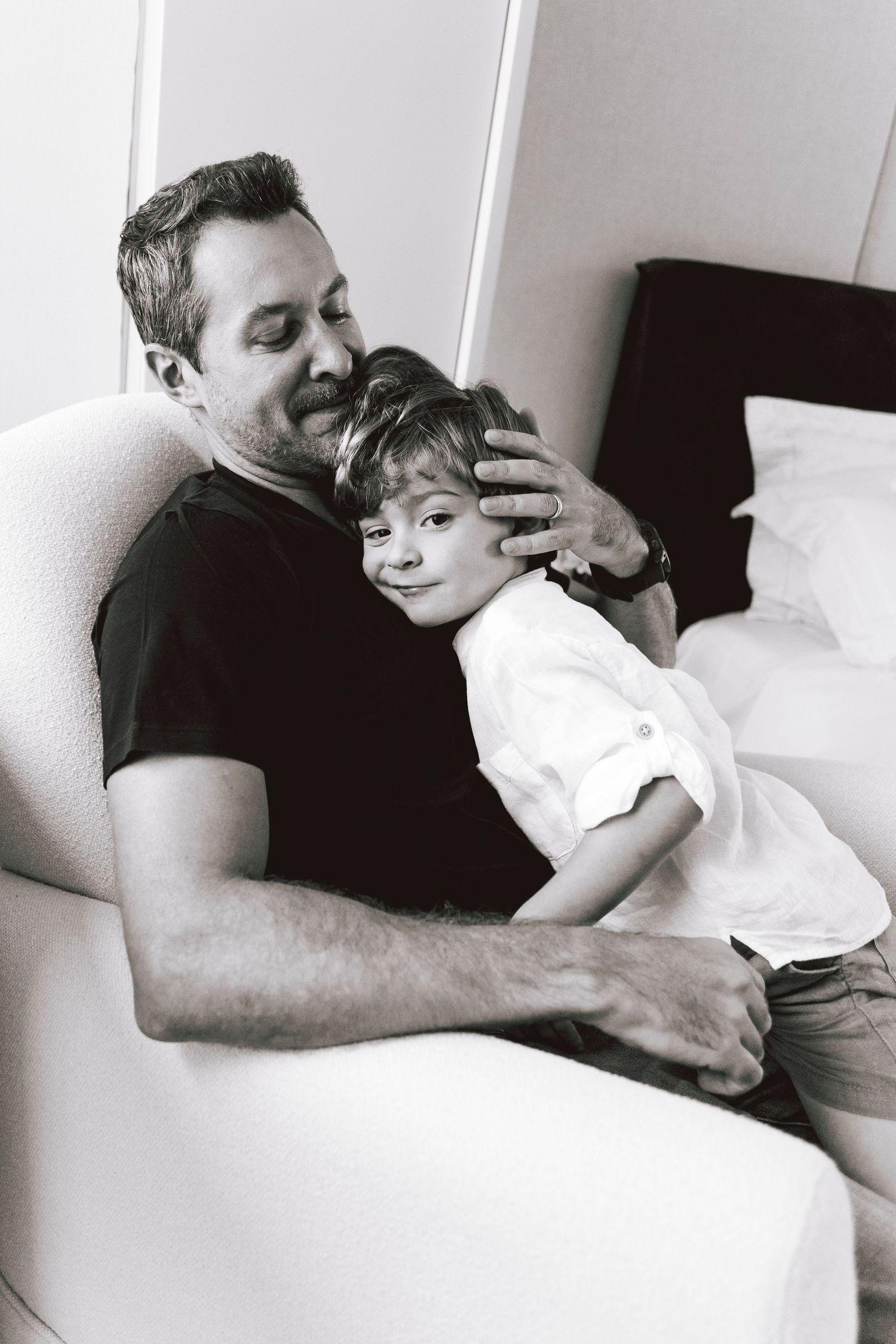Tender black and white portrait of parent and child embracing on white chair.