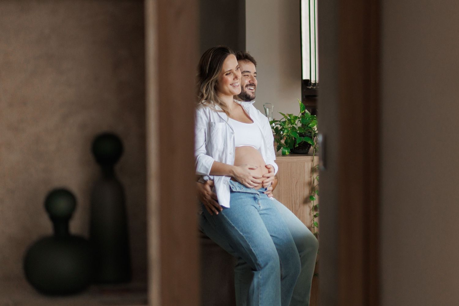 Happy couple expecting a baby, woman showing pregnant belly, smiling together in a modern home interior.
