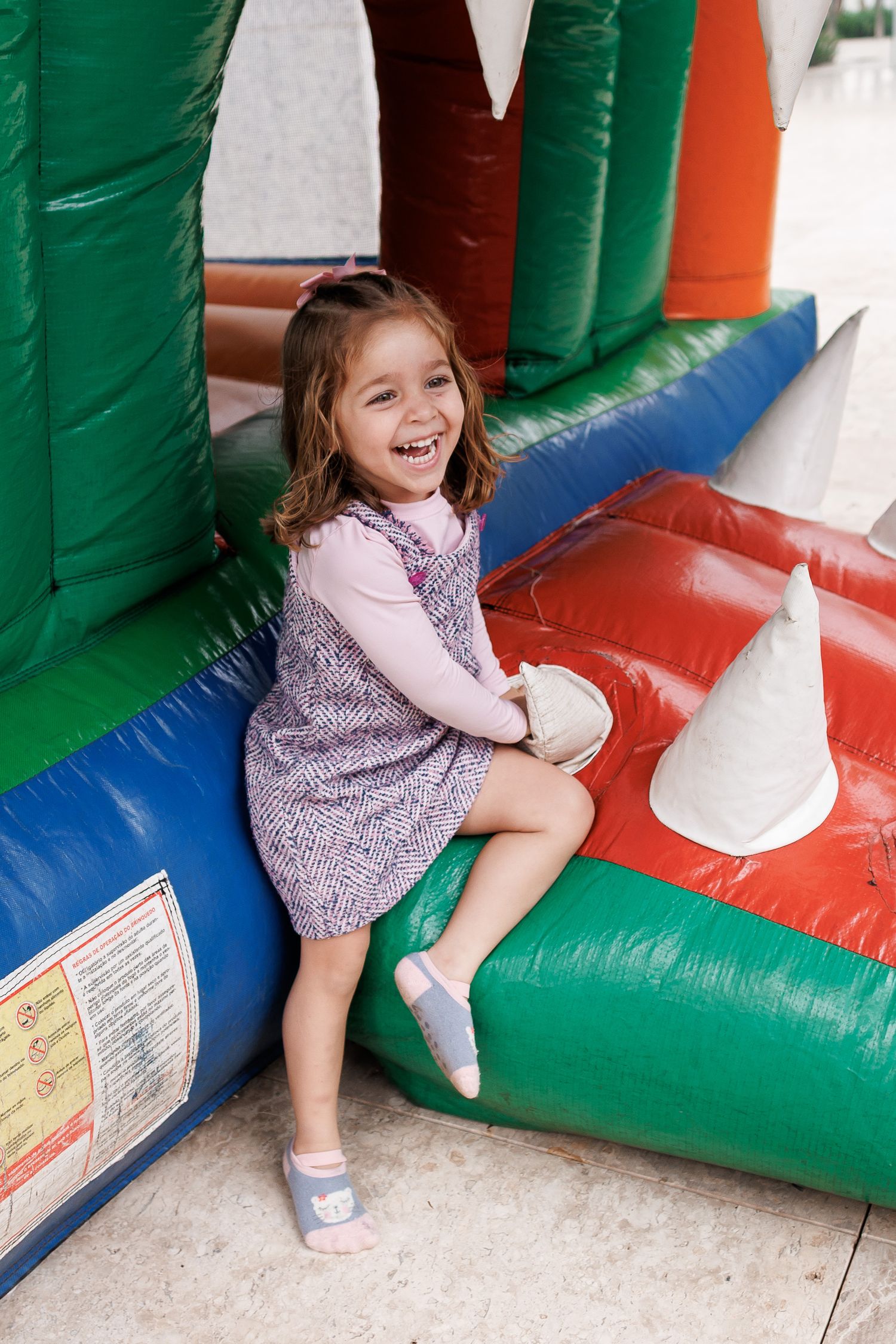 A child plays and laughs while sitting in a colorful inflatable bounce house with green, red and blue sections.