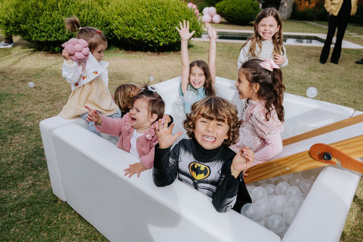 Children play together in a white outdoor bathtub filled with bubbles during a sunny day.
