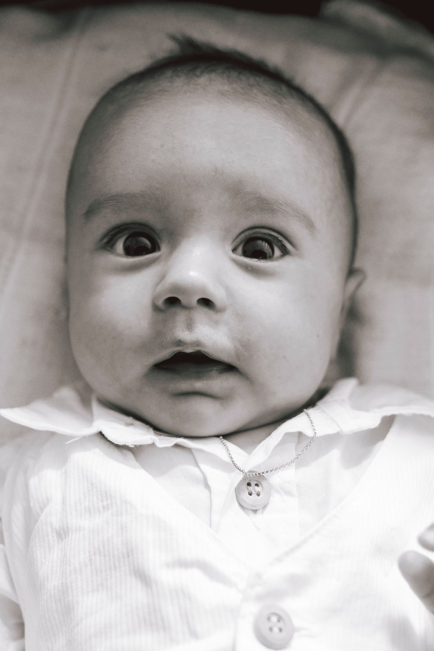 A black and white close-up portrait of a baby wearing a white buttoned shirt with wide curious eyes.