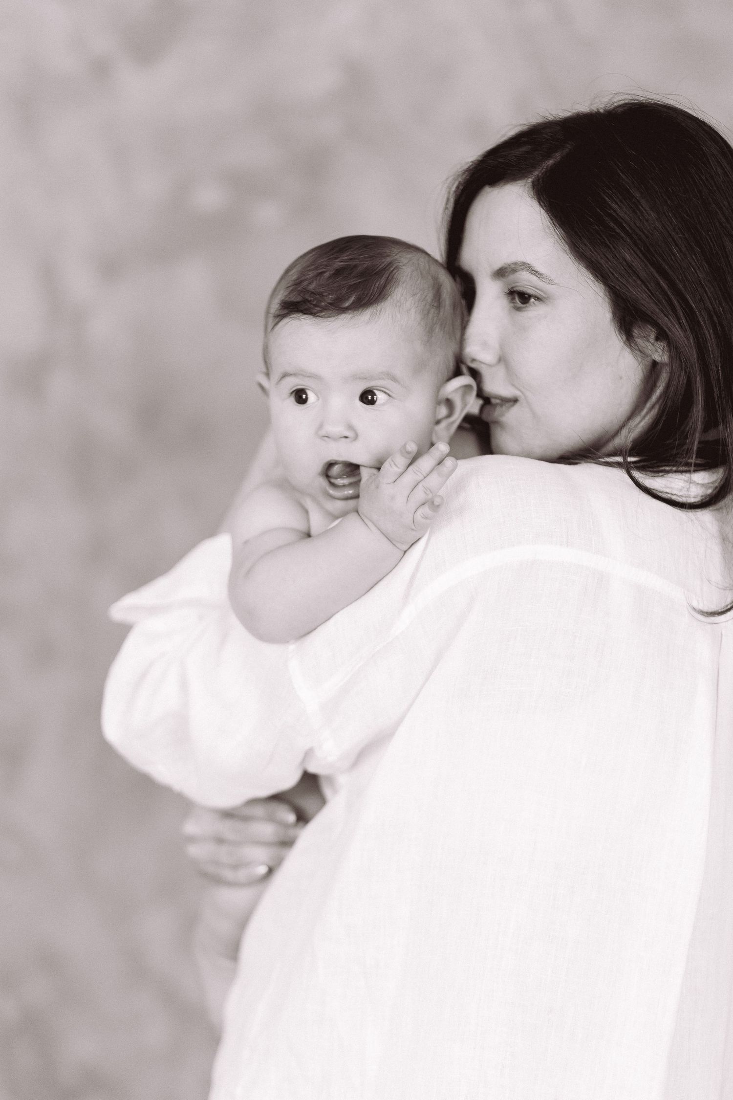 Black and white photo of a mother in white shirt tenderly holding her wide-eyed baby close to her face.