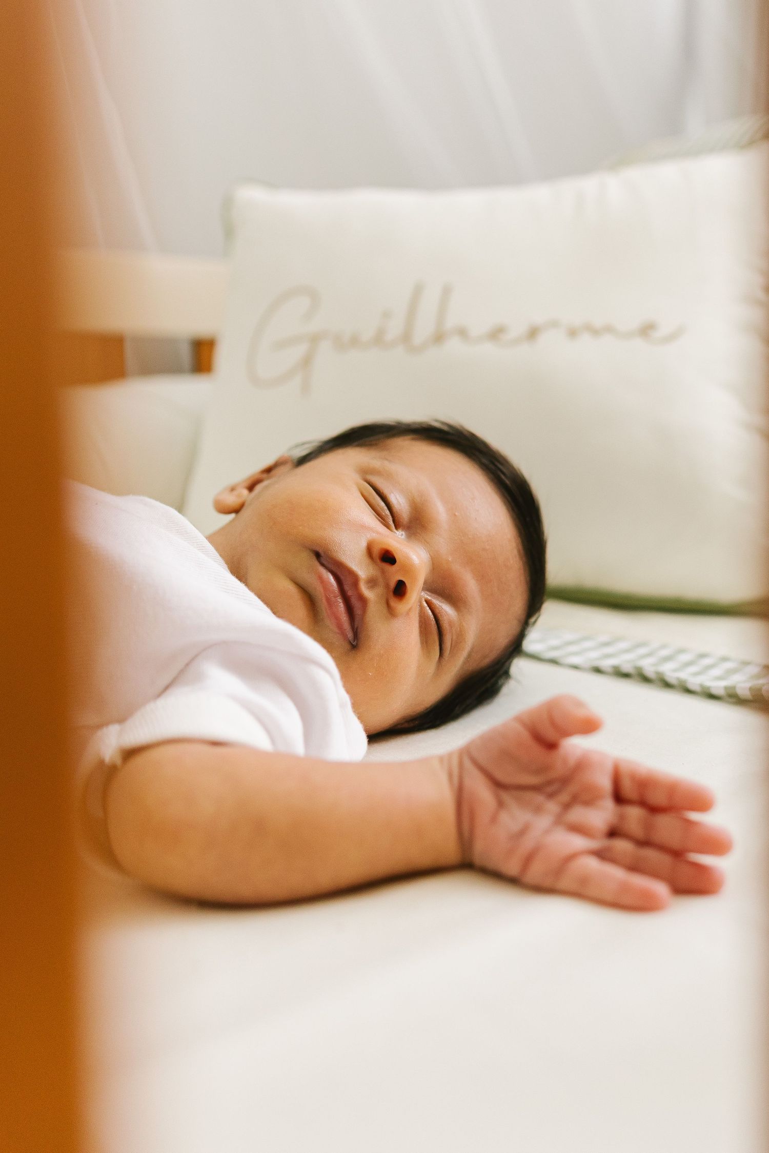 Newborn baby Guilherme sleeping peacefully in a white crib with a personalized name pillow.
