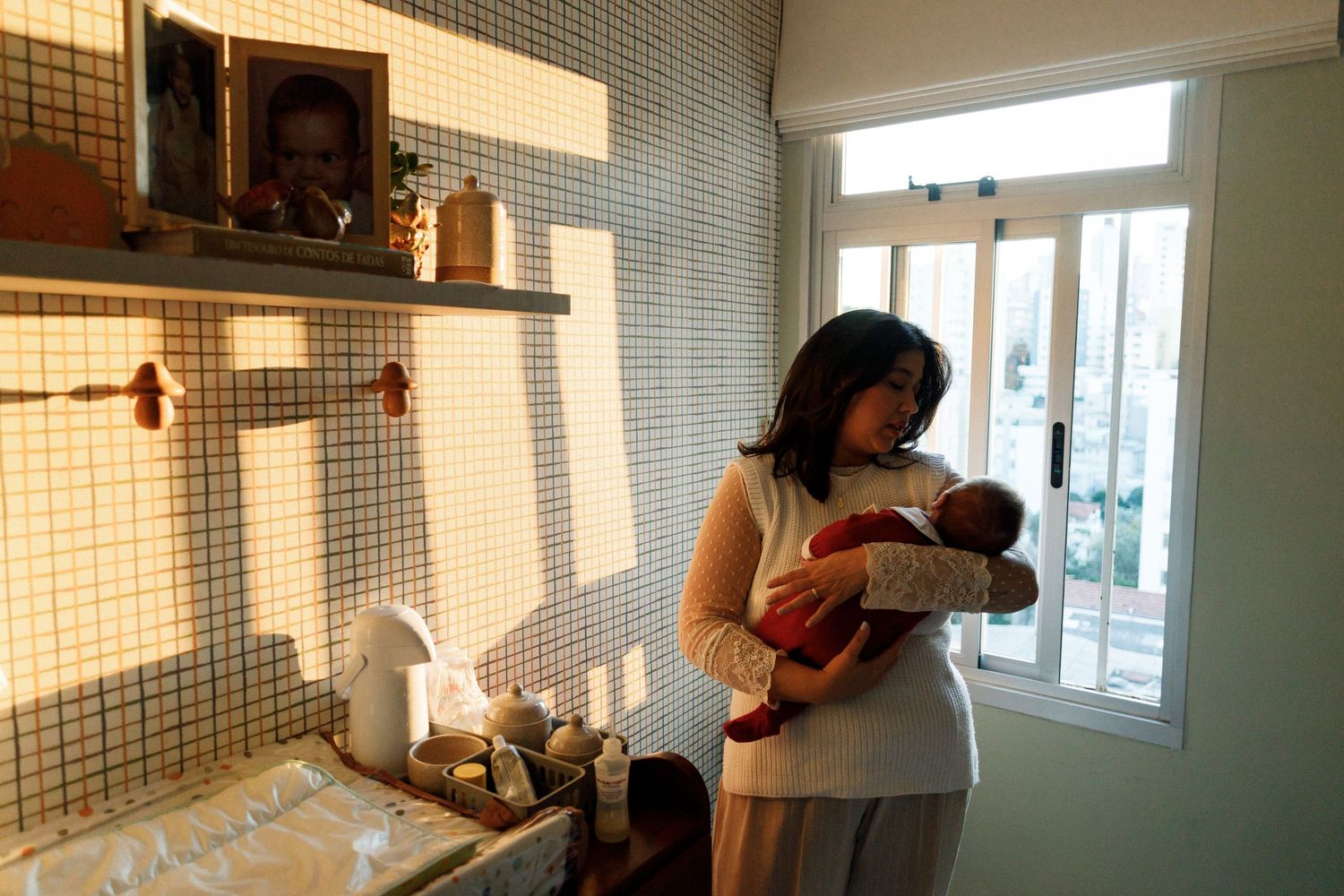 Woman cradling newborn baby in a cozy tiled kitchen with warm natural light streaming through a window.