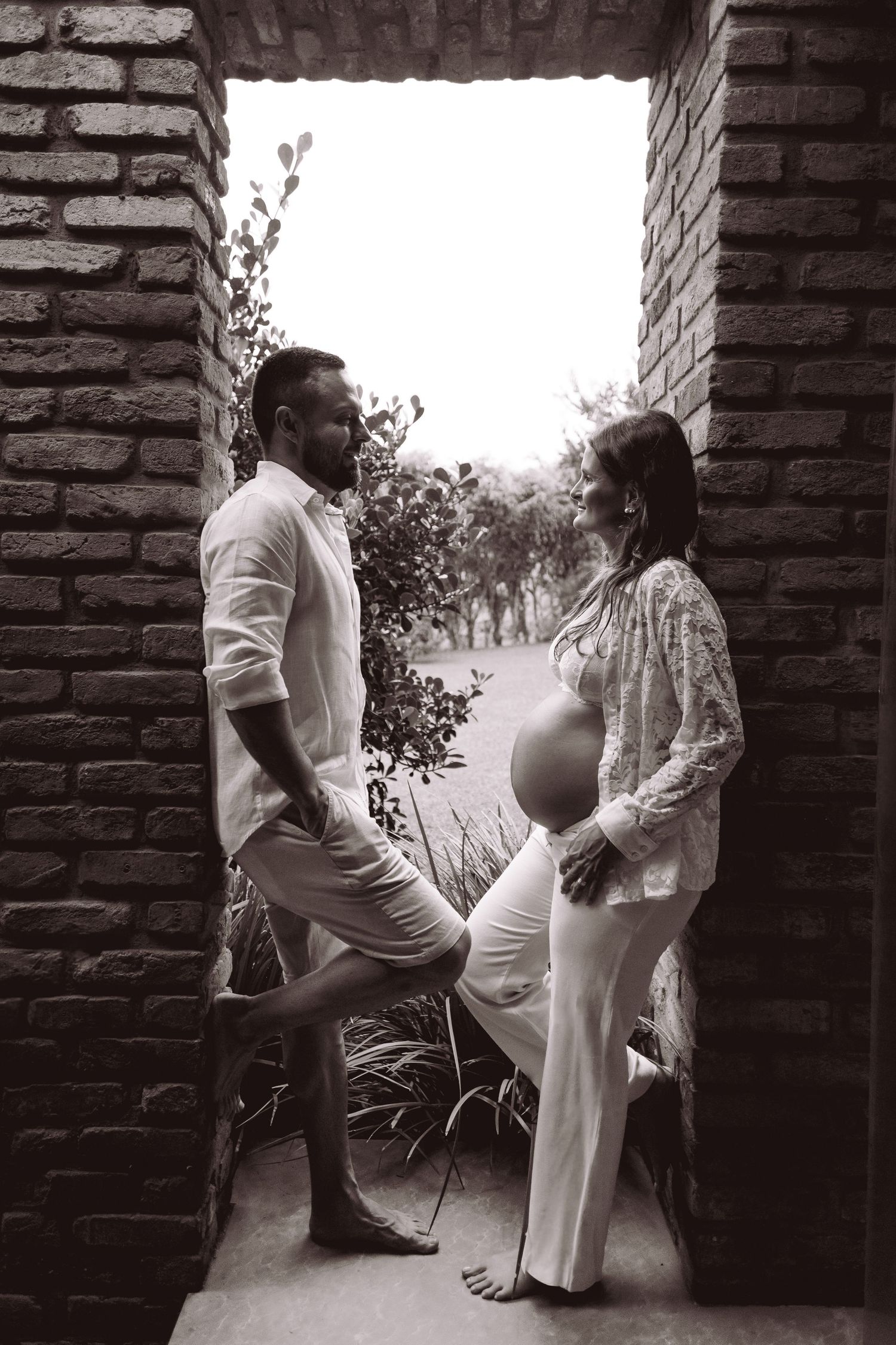 Black and white maternity photo of couple facing each other in rustic brick doorway.