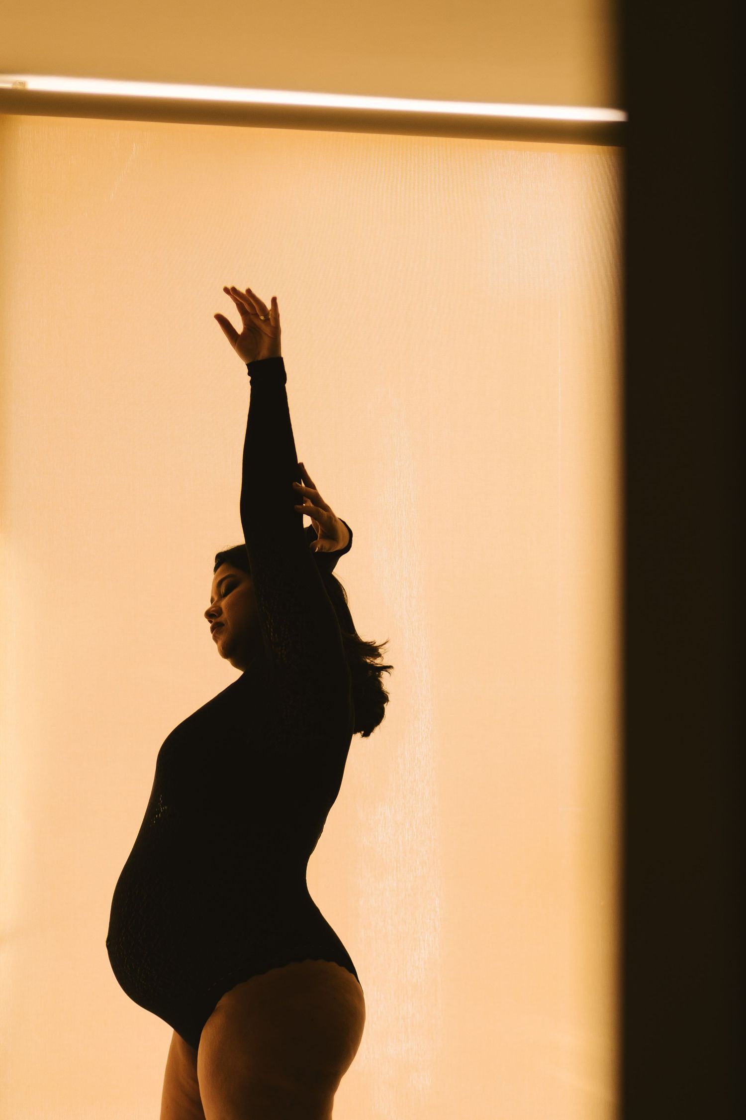 Silhouette of a woman in a black bodysuit striking a graceful pose with arm raised against a warm golden background.