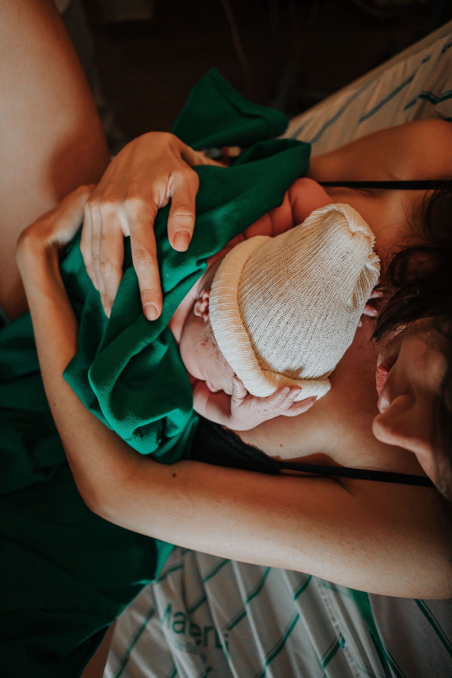 Intimate moment with newborn wearing knit cap against green hospital linens.