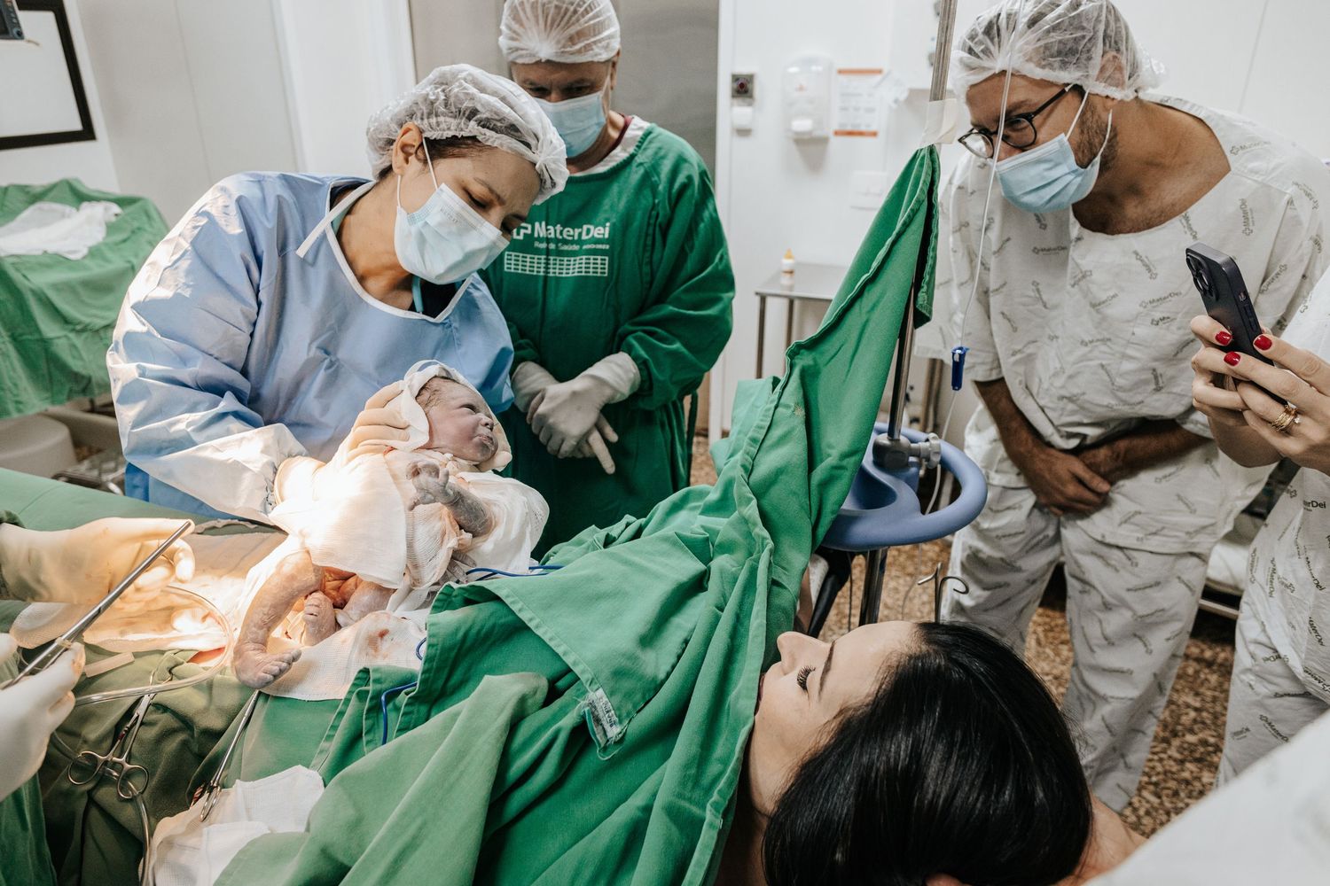 Medical team performing delivery procedure in operating room with green surgical drapes.