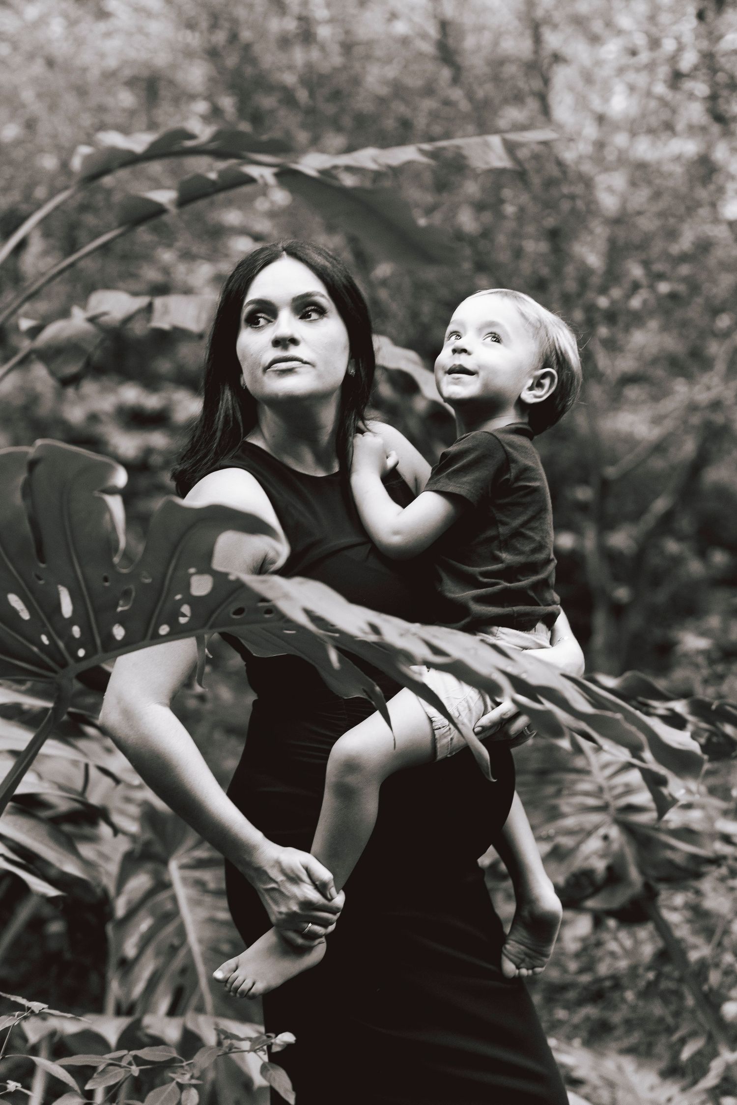 Black and white photo of mother and child surrounded by large tropical leaves in garden setting.